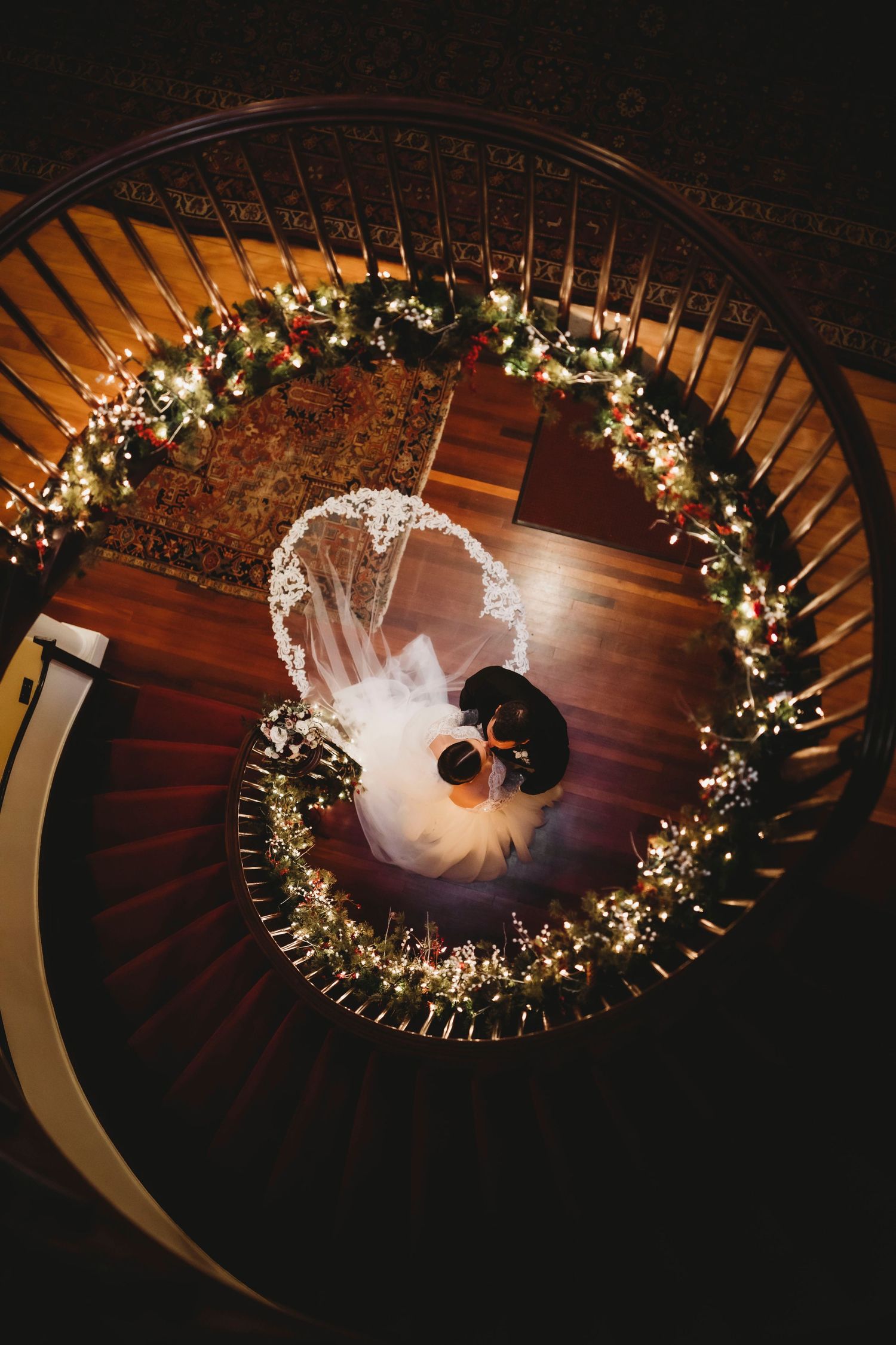 Aerial view of a spiral staircase decorated with floral arrangements and a flowing white dress creating a dramatic pattern.