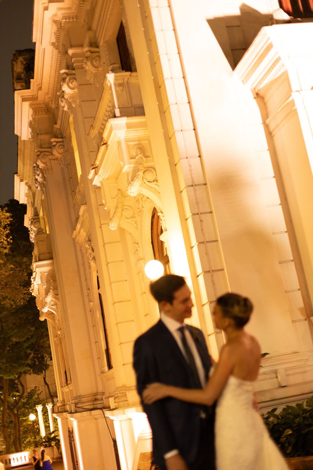 Romantic evening wedding scene with couple dancing on illuminated white columned porch at dusk.