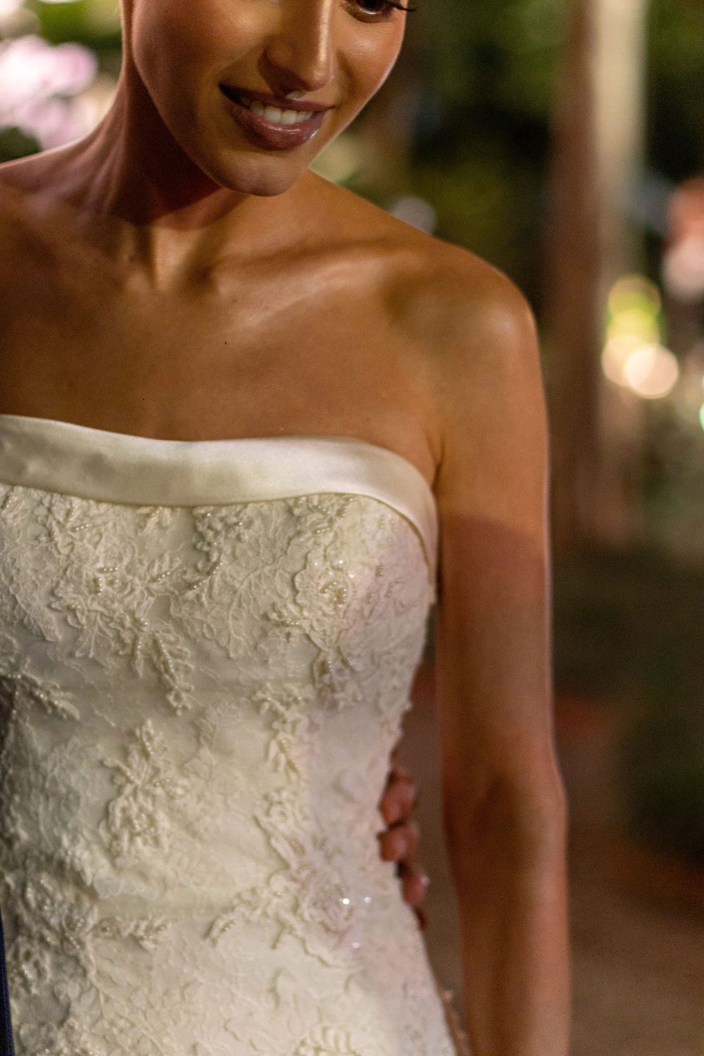 Close-up view of a strapless wedding dress with delicate lace embroidery and beading details.