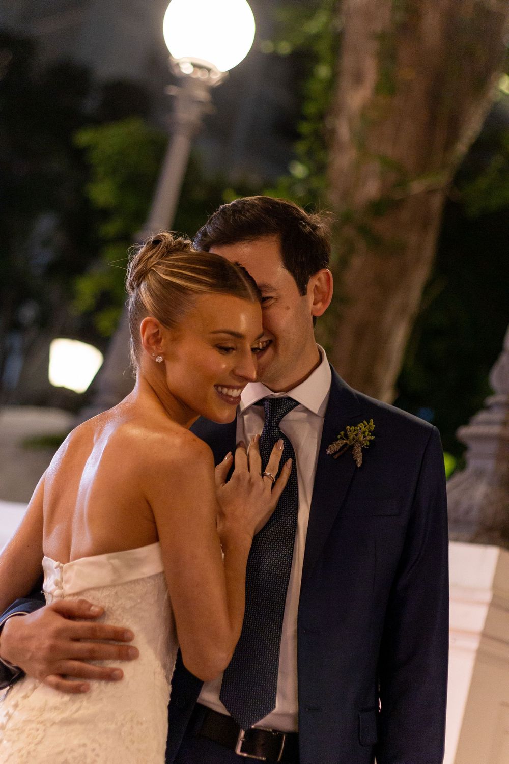 A romantic moment between newlyweds sharing a laugh under glowing lights at an evening wedding reception.