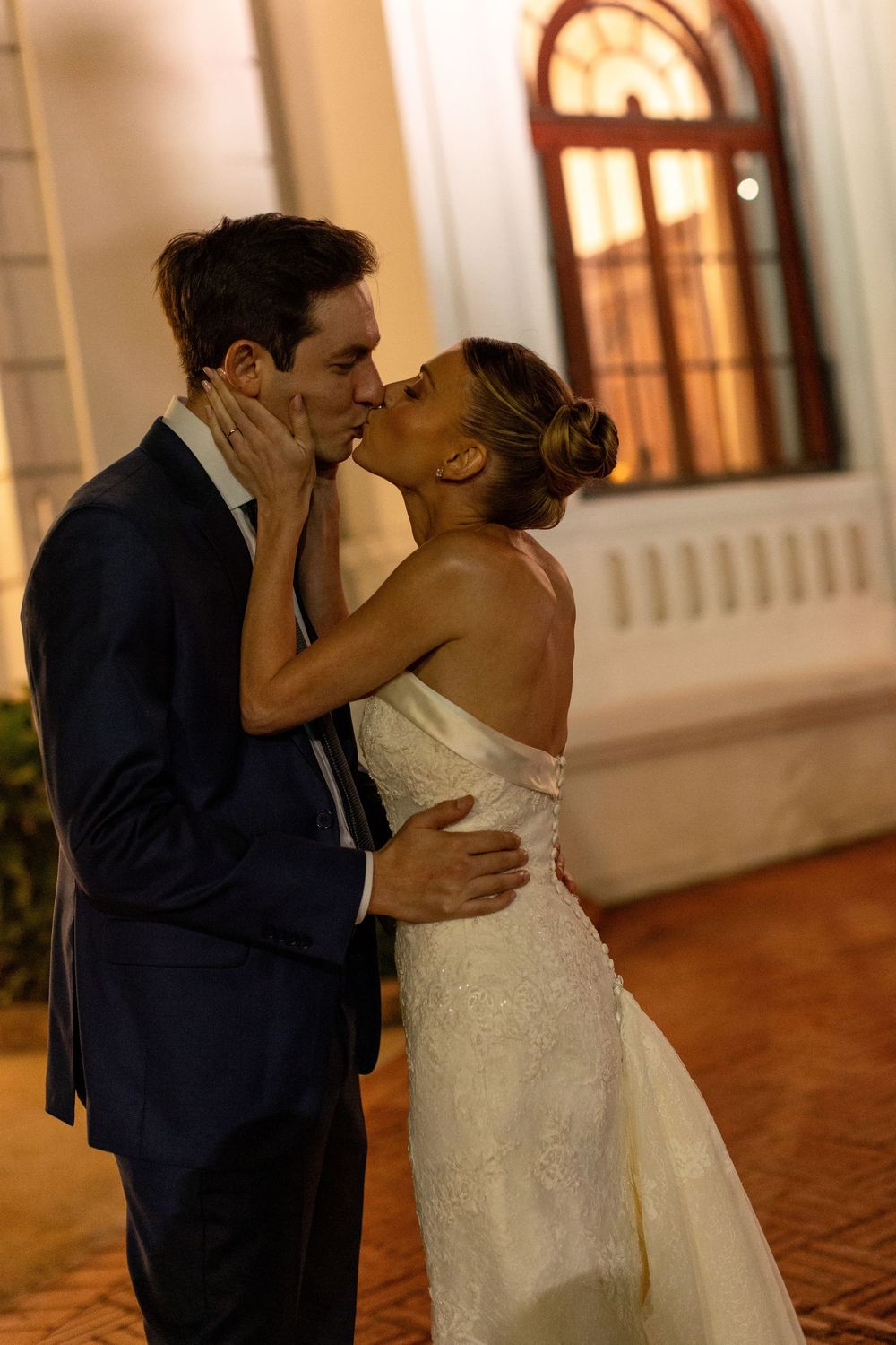 A bride and groom share a romantic kiss sequence in an elegant venue with warm lighting and white columns.