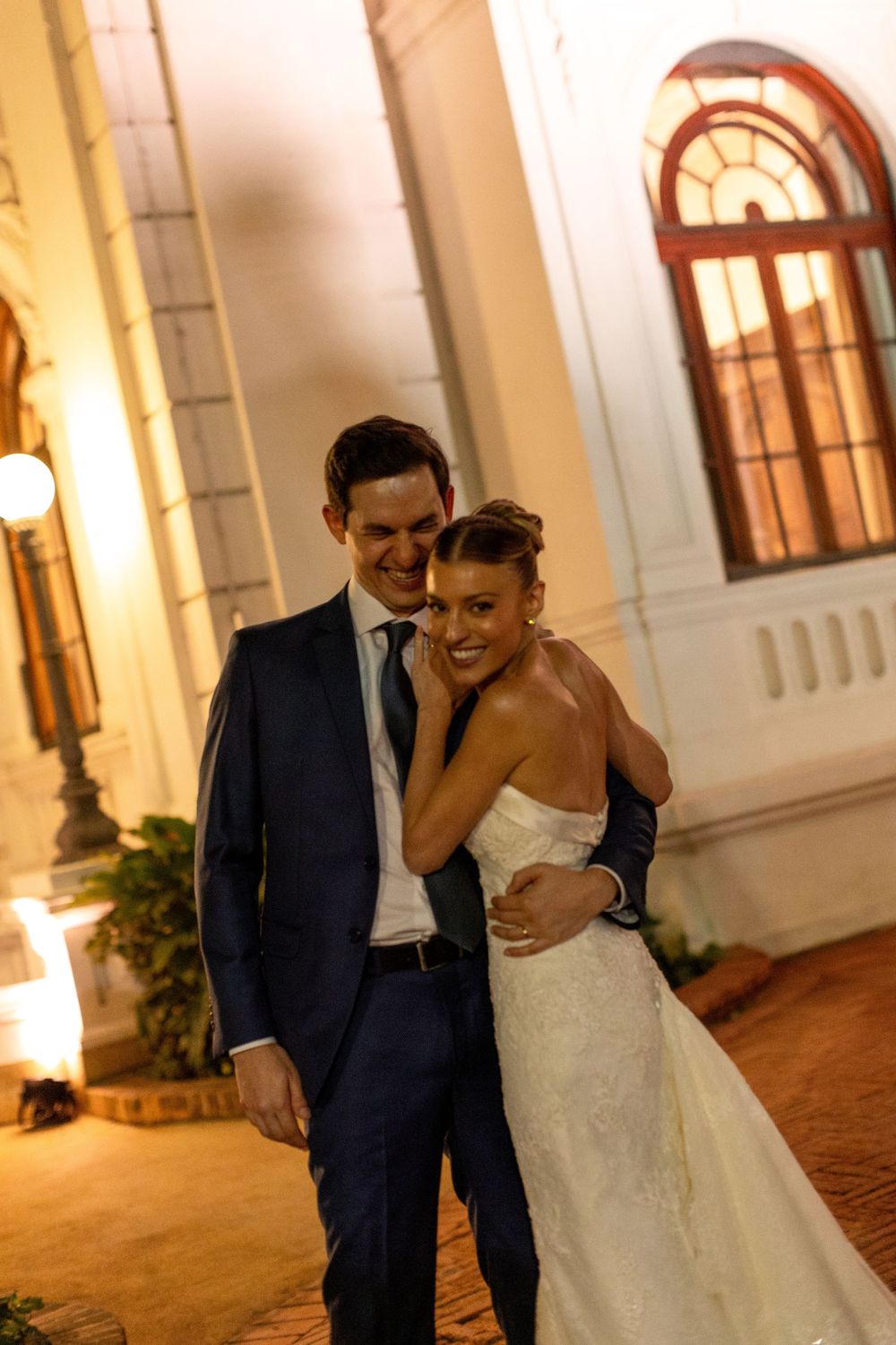 A couple shares an intimate moment while walking along an elegant colonnade at dusk.