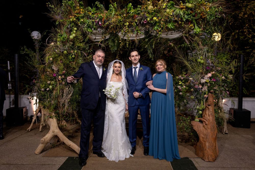 Wedding party poses together in an outdoor garden setting with lush greenery and decorative lighting.