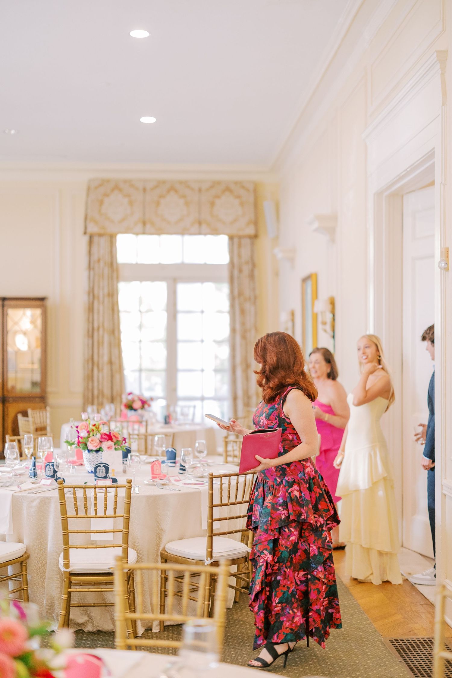 Elegant white wedding venue room with gold chairs and pink floral centerpieces set for a reception celebration.