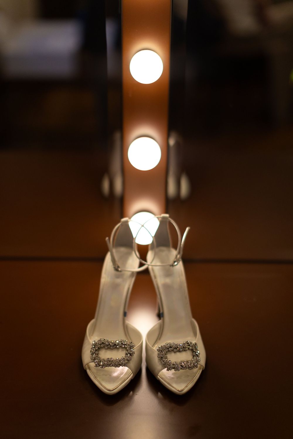 Elegant white bridal shoes with crystal embellishments displayed under soft lighting.