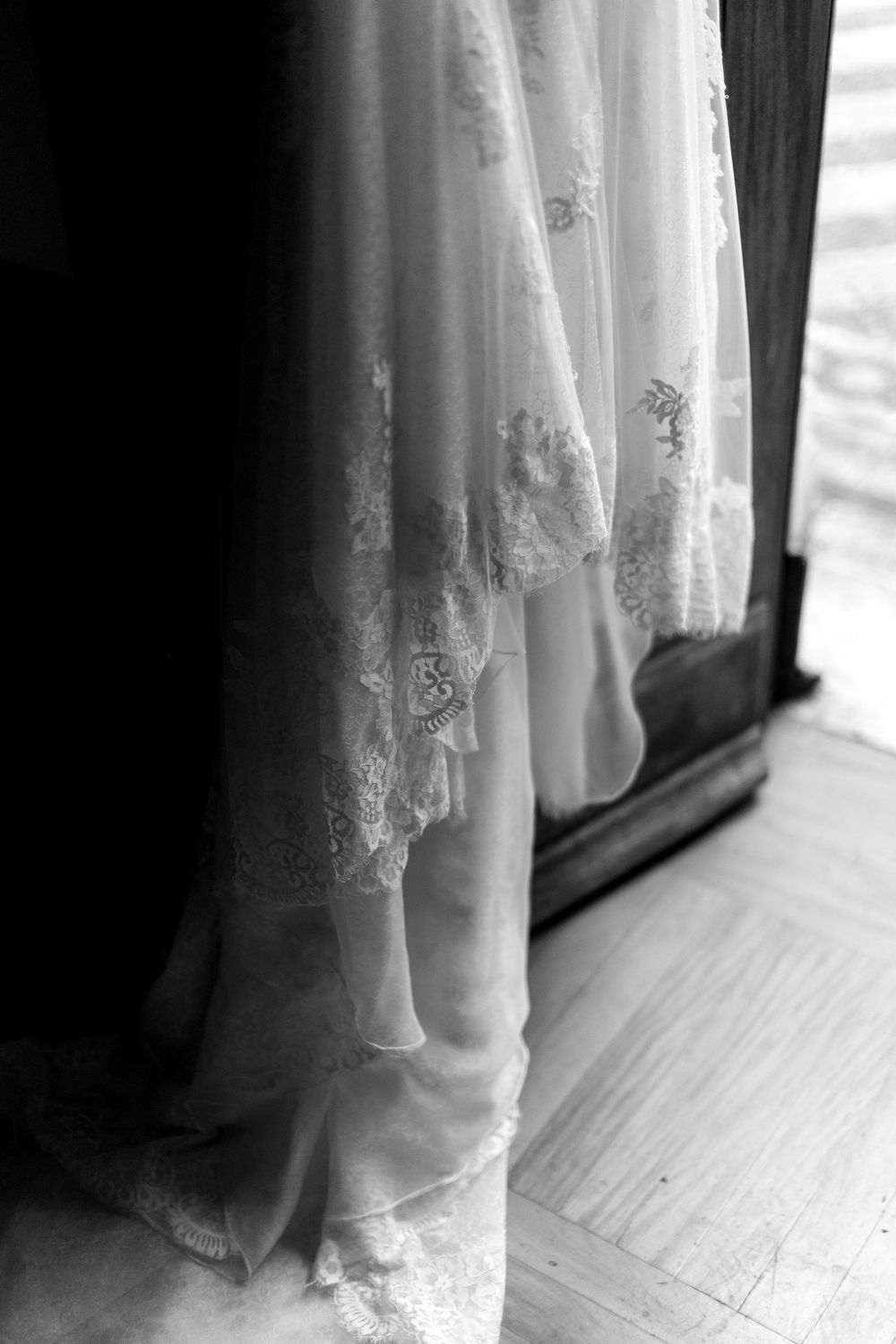 Close-up detail of delicate lace trim on a white wedding dress veil against a hardwood floor.