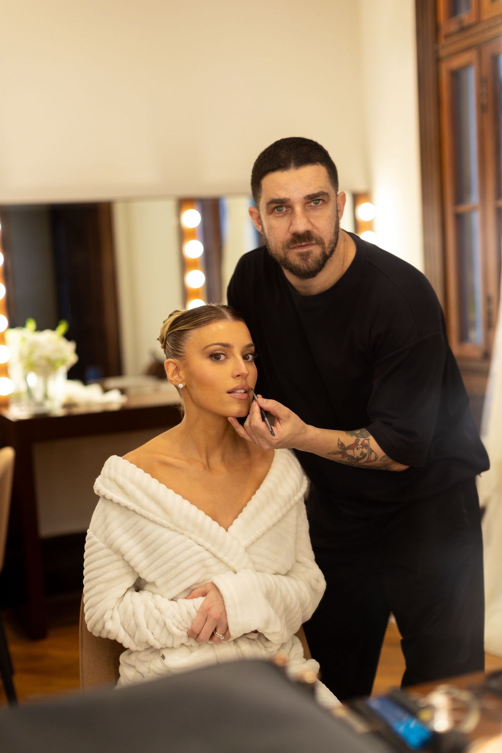 Makeup artist applying cosmetics to someone in a white robe during wedding preparations.