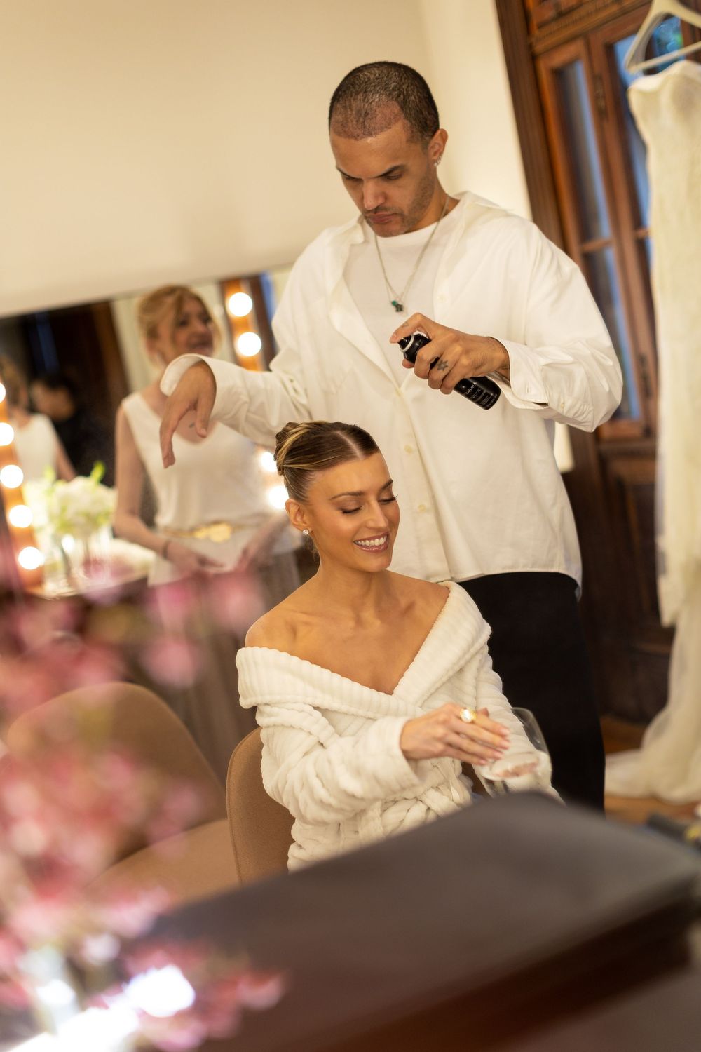 Wedding reception scene with guests in white attire gathered around a dining table with pink floral decor.