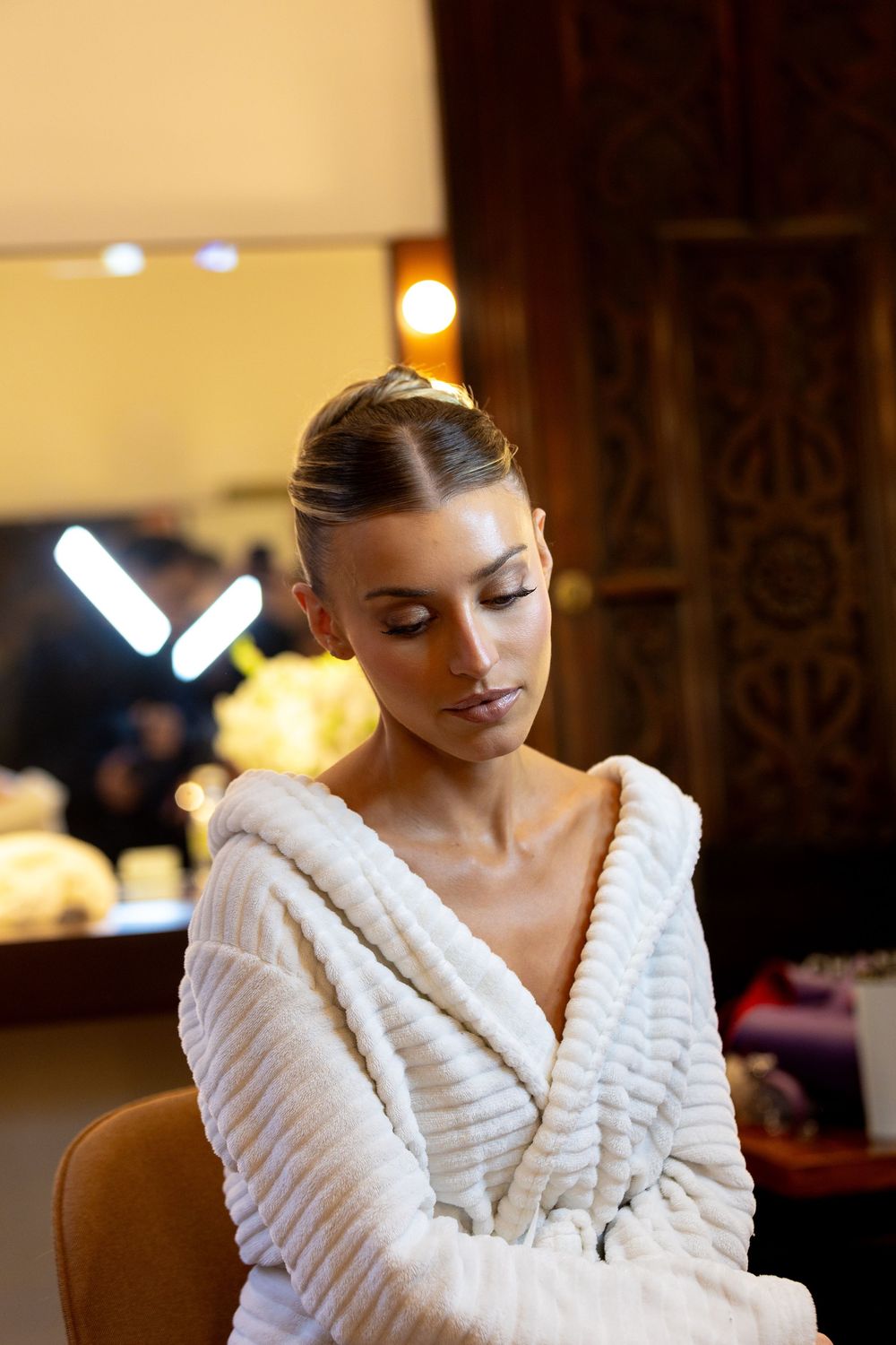 A person wearing a plush white robe sits in warm lighting during wedding day preparations.