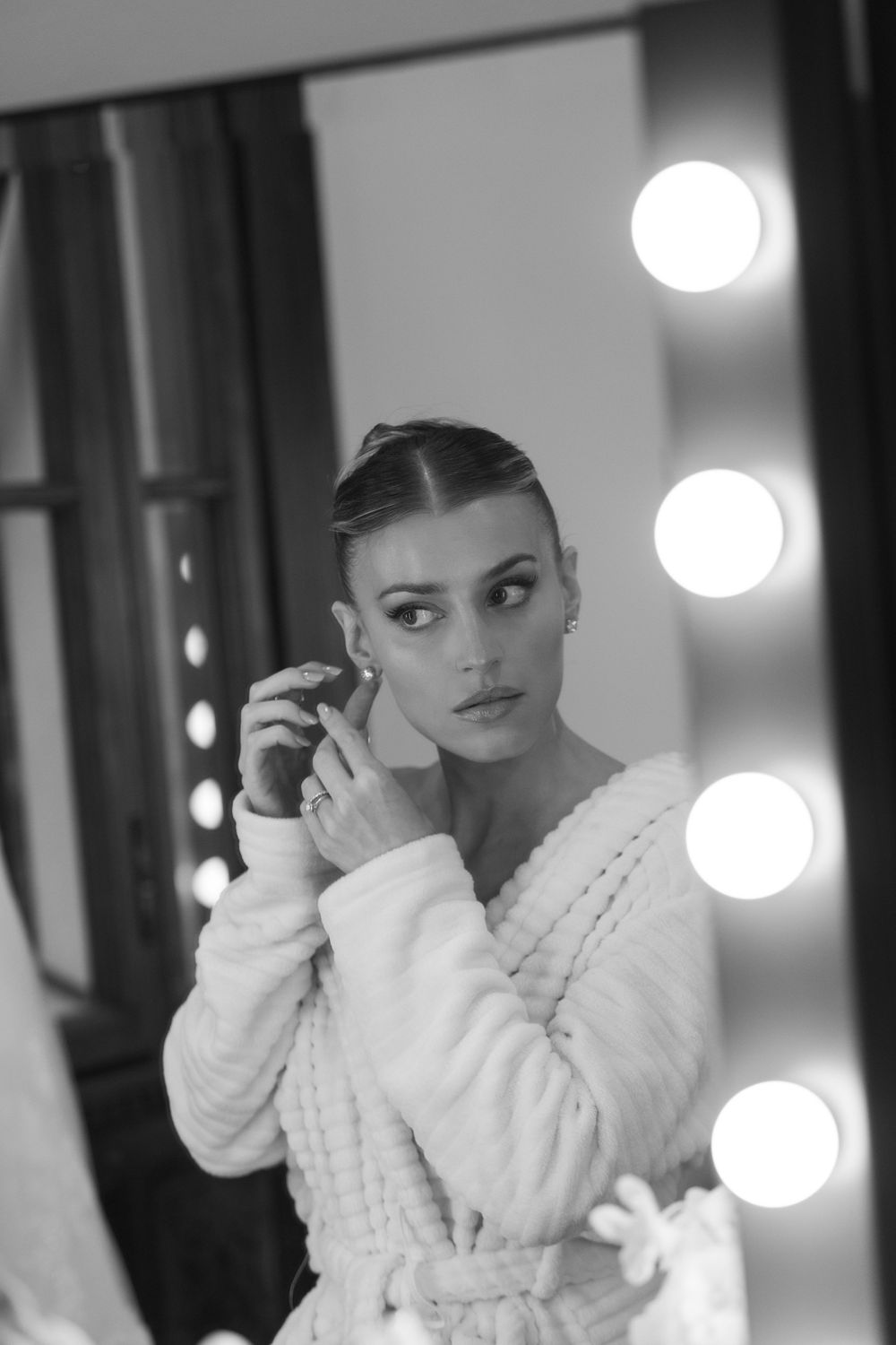Artistic black and white photos showing someone in a white robe getting ready in front of vanity lights.