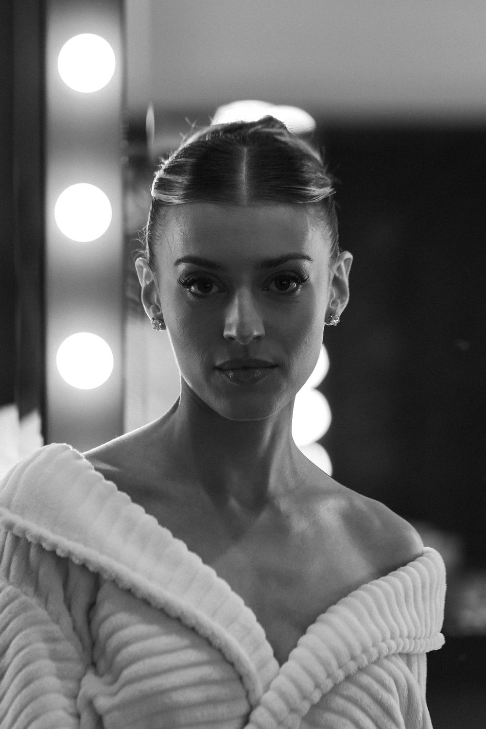 Black and white portrait sequence showing a dancer in a white robe with vanity lights in the background.