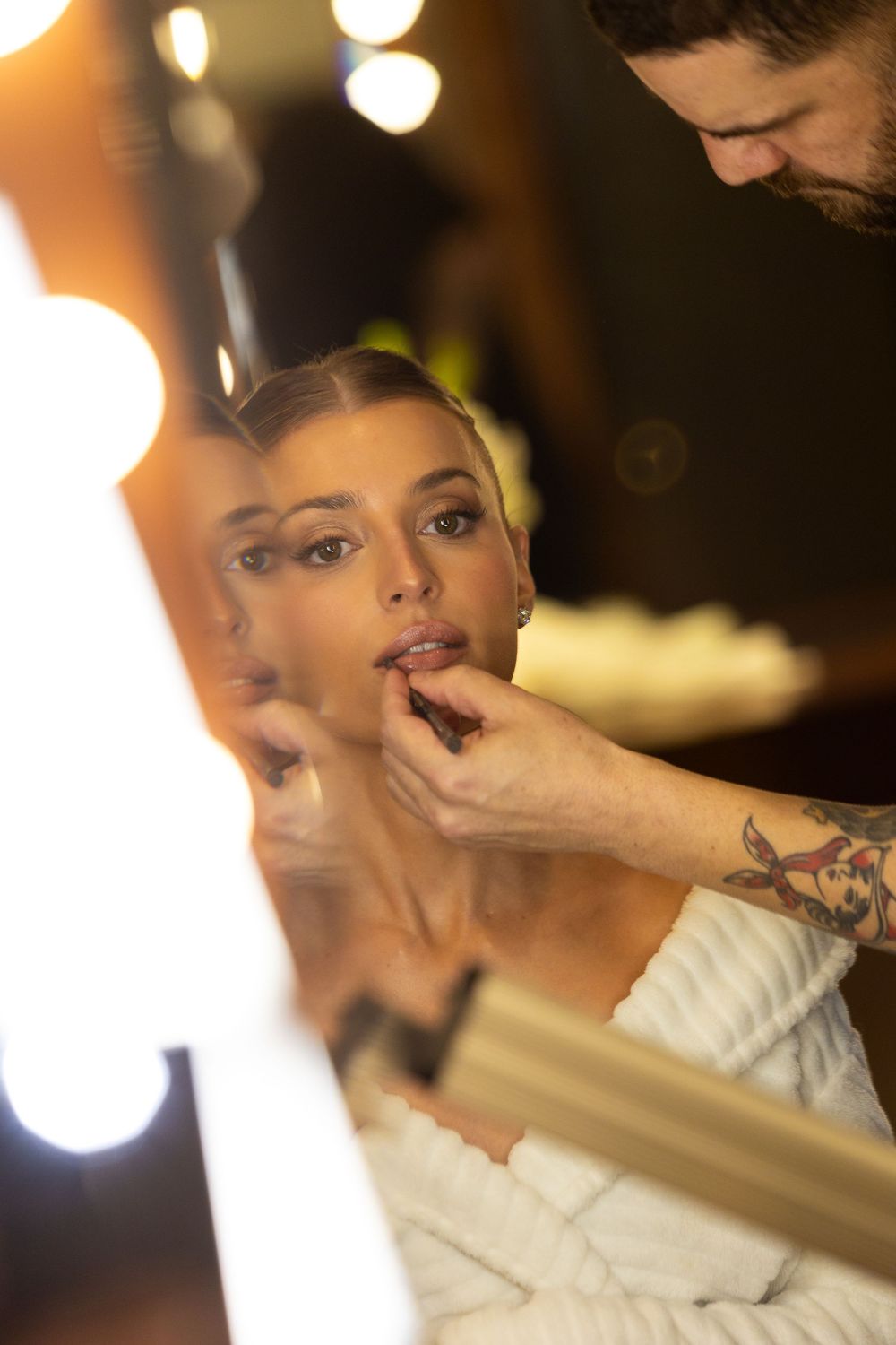 Makeup artist applies finishing touches during wedding preparations in warm lighting.