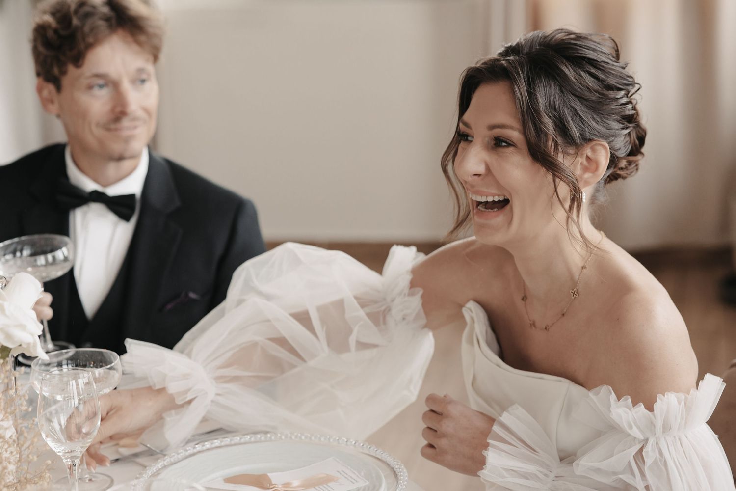 A laughing bride in a white strapless wedding dress shares a joyful moment during celebration.