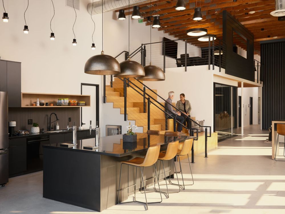 Modern coworking kitchen with island bar seating and pendant lighting — architectural interior by Khoi Ly.