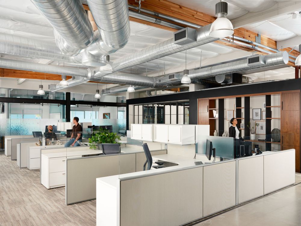 Open-plan office interior with exposed ceiling ducts, cubicle layout, and industrial design — commercial architecture by Khoi Ly.