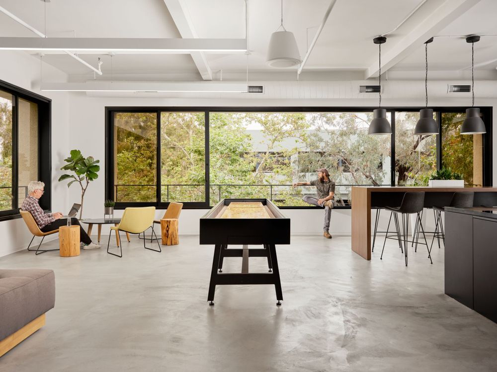 Game and lounge room with foosball table, large windows, and open kitchen — creative office space by Khoi Ly.