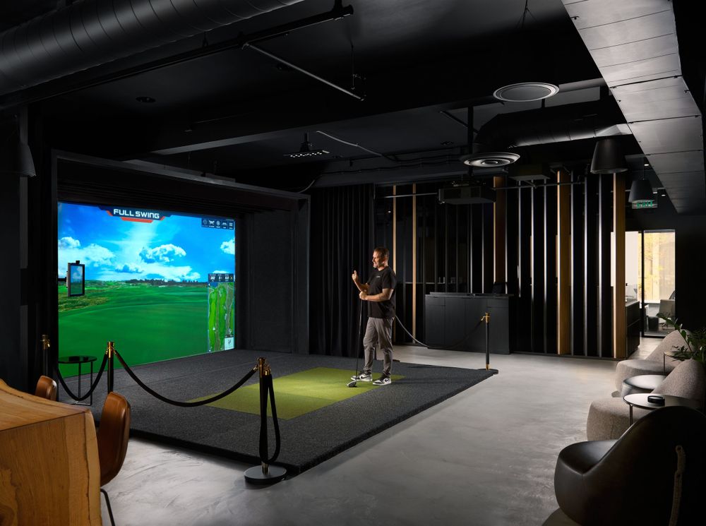 Indoor golf simulator room with lounge seating and dark moody lighting — photographed by Khoi Ly at Camino office.