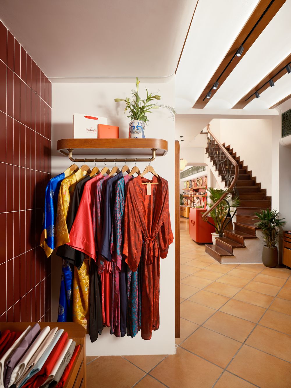 Display corner of silk garments with rich colors and staircase view — captured by Khoi Ly in a Vietnamese boutique.