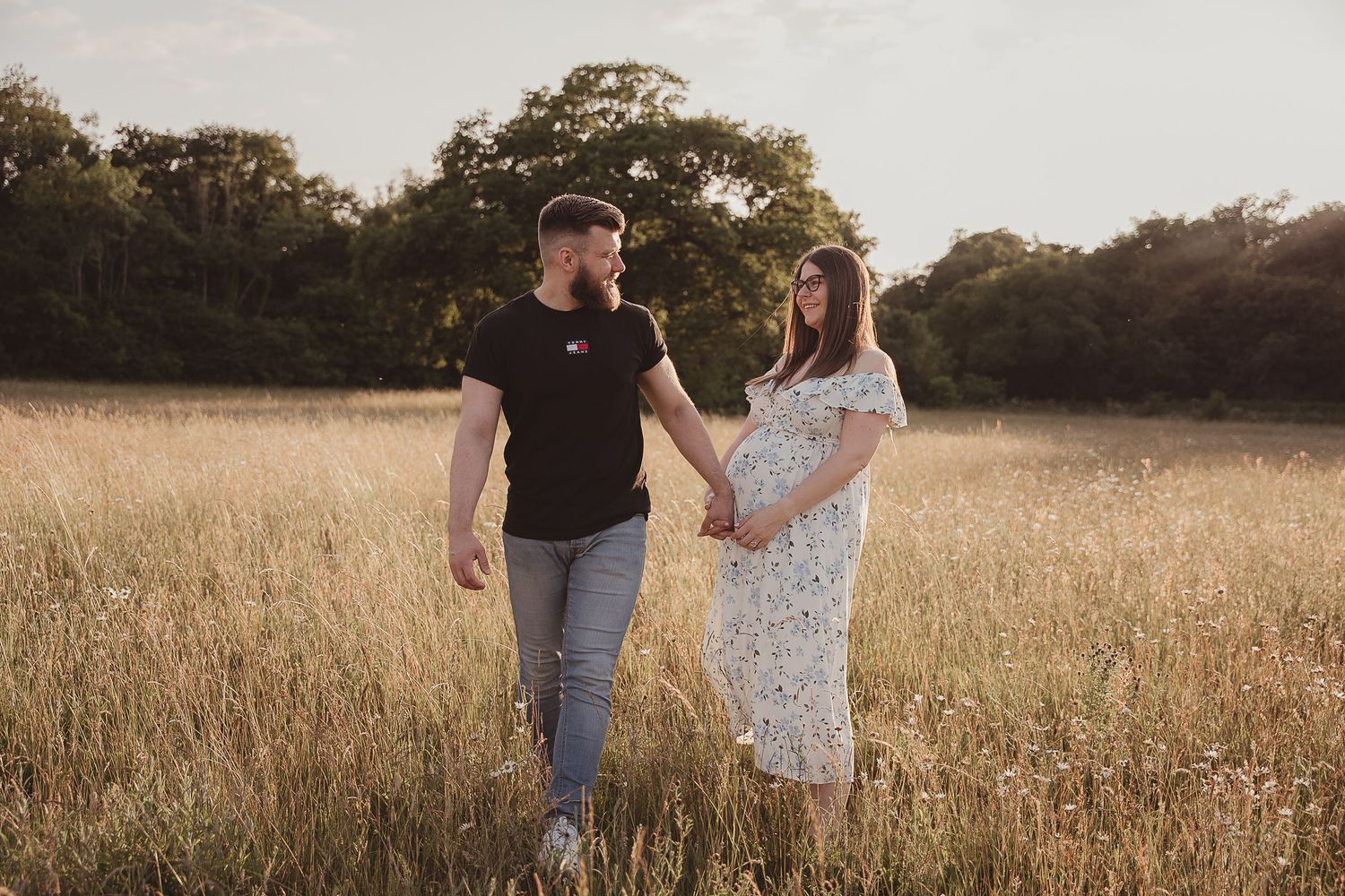 Two people walk through a golden field at sunset holding hands and a map.