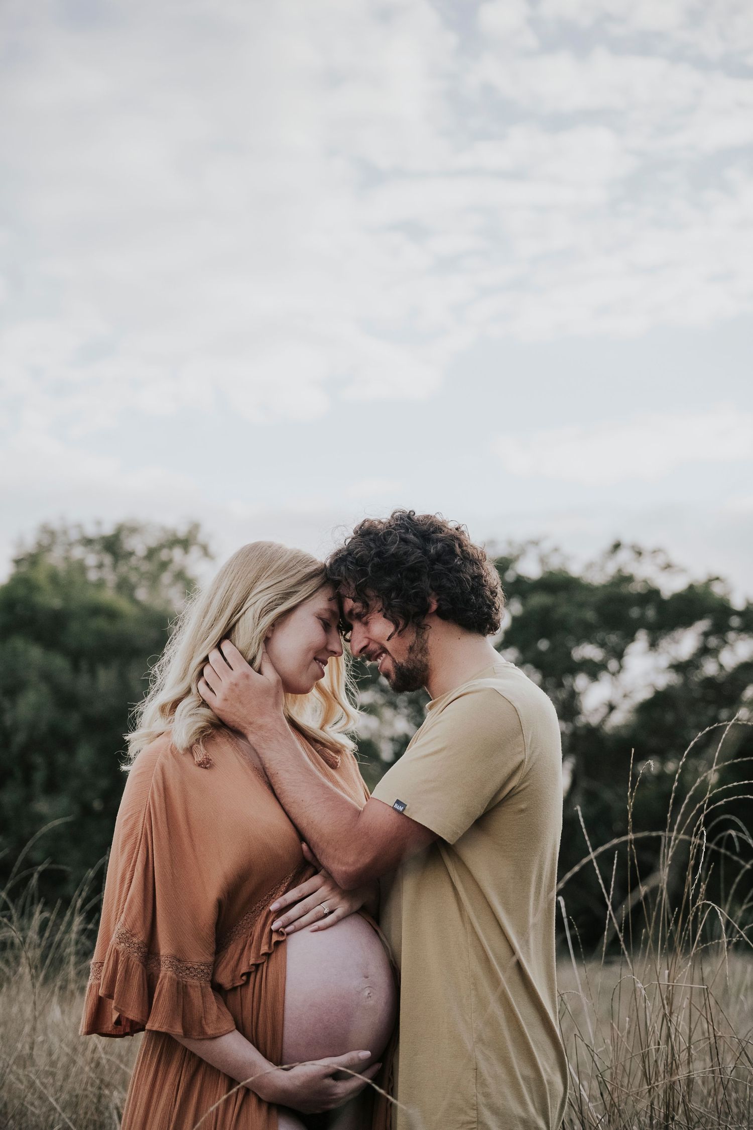 Intimate maternity photo of couple sharing tender moment together in golden field at sunset.