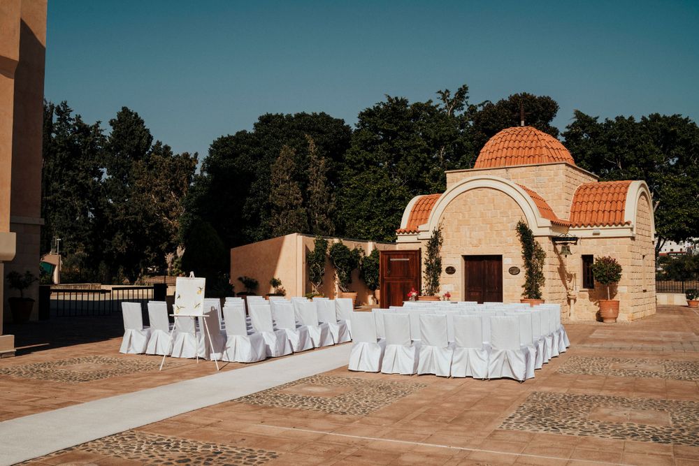 Outdoor wedding ceremony setup with white chairs facing a Mediterranean-style chapel with terracotta domes.