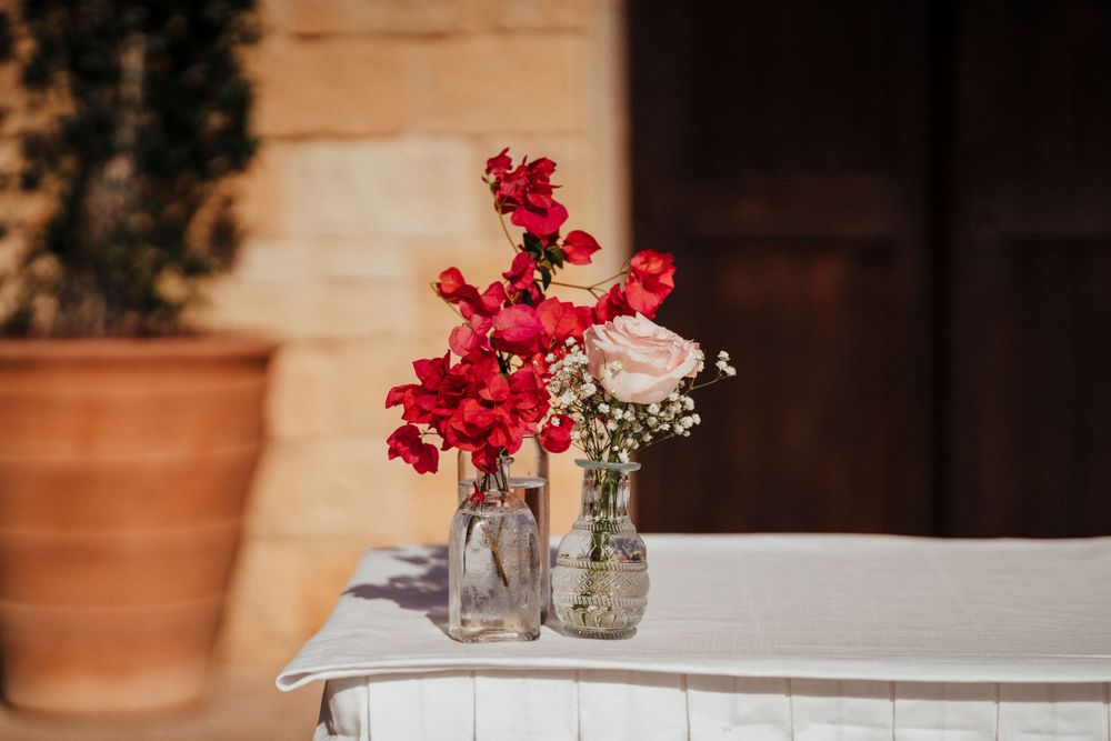 Simple floral arrangement with red snapdragons and baby's breath in glass mason jars on white surface.
