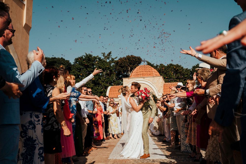 Wedding celebration with guests throwing confetti during a joyful exit ceremony at an outdoor venue.