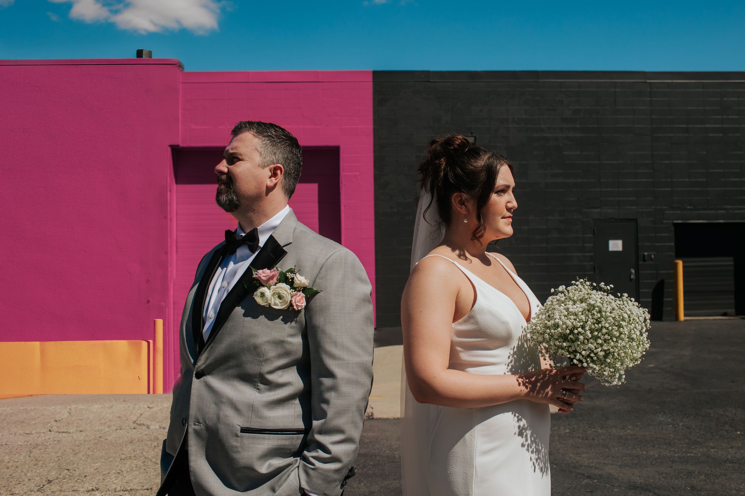 A wedding couple stands against colorful walls in an urban setting with pink and blue backdrops in Indianapolis Indiana.