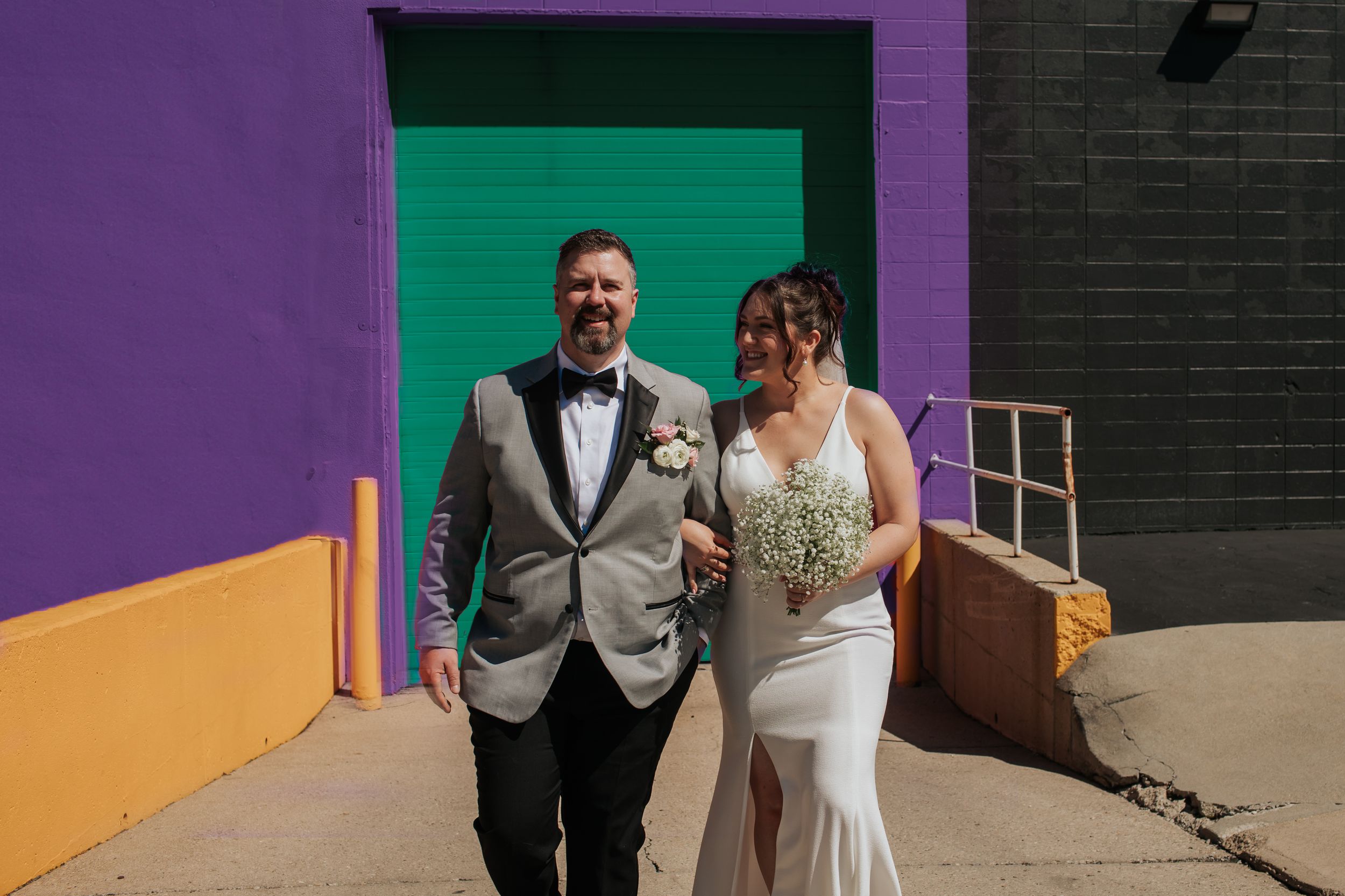 A couple shares a joyful moment together in front of a colorful wall with purple and teal accents in Indianapolis Indiana.