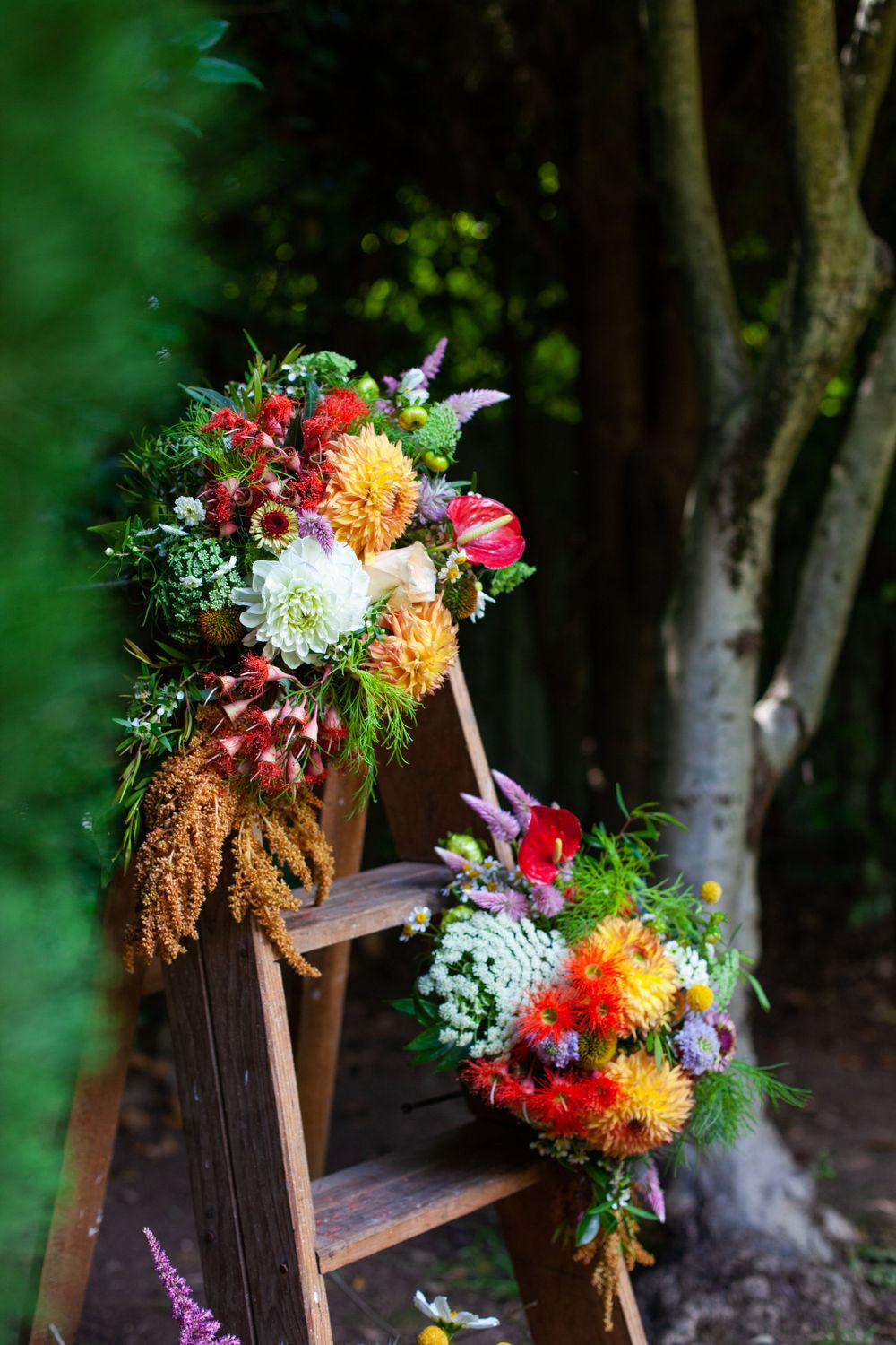 Two vibrant autumn flower bouquets with dahlias and wildflowers arranged on wooden ladder steps in a garden setting.