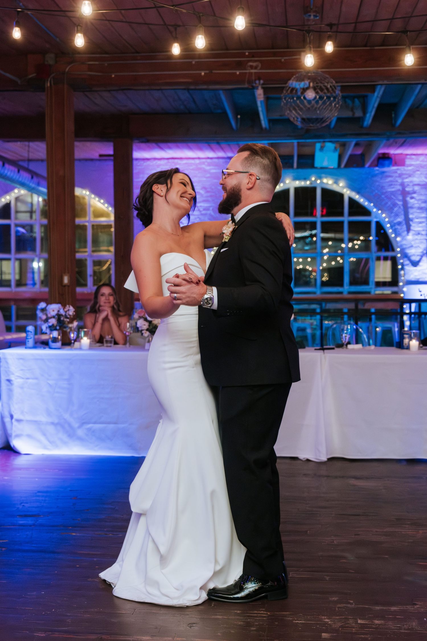 A couple shares their first dance at their elegant wedding reception with purple and blue ambient lighting.