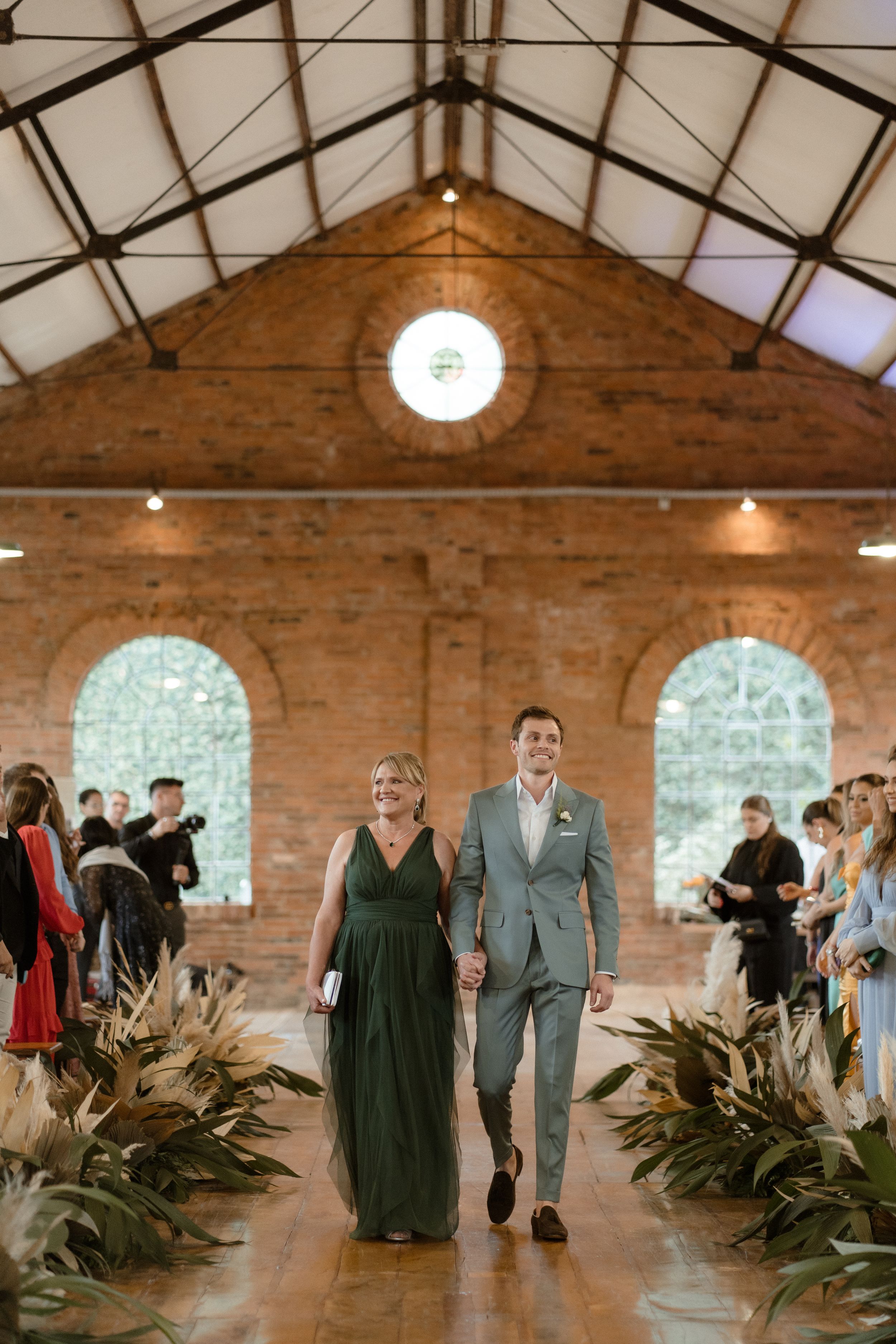 Wedding processional in a rustic brick venue with tropical plants lining the aisle.