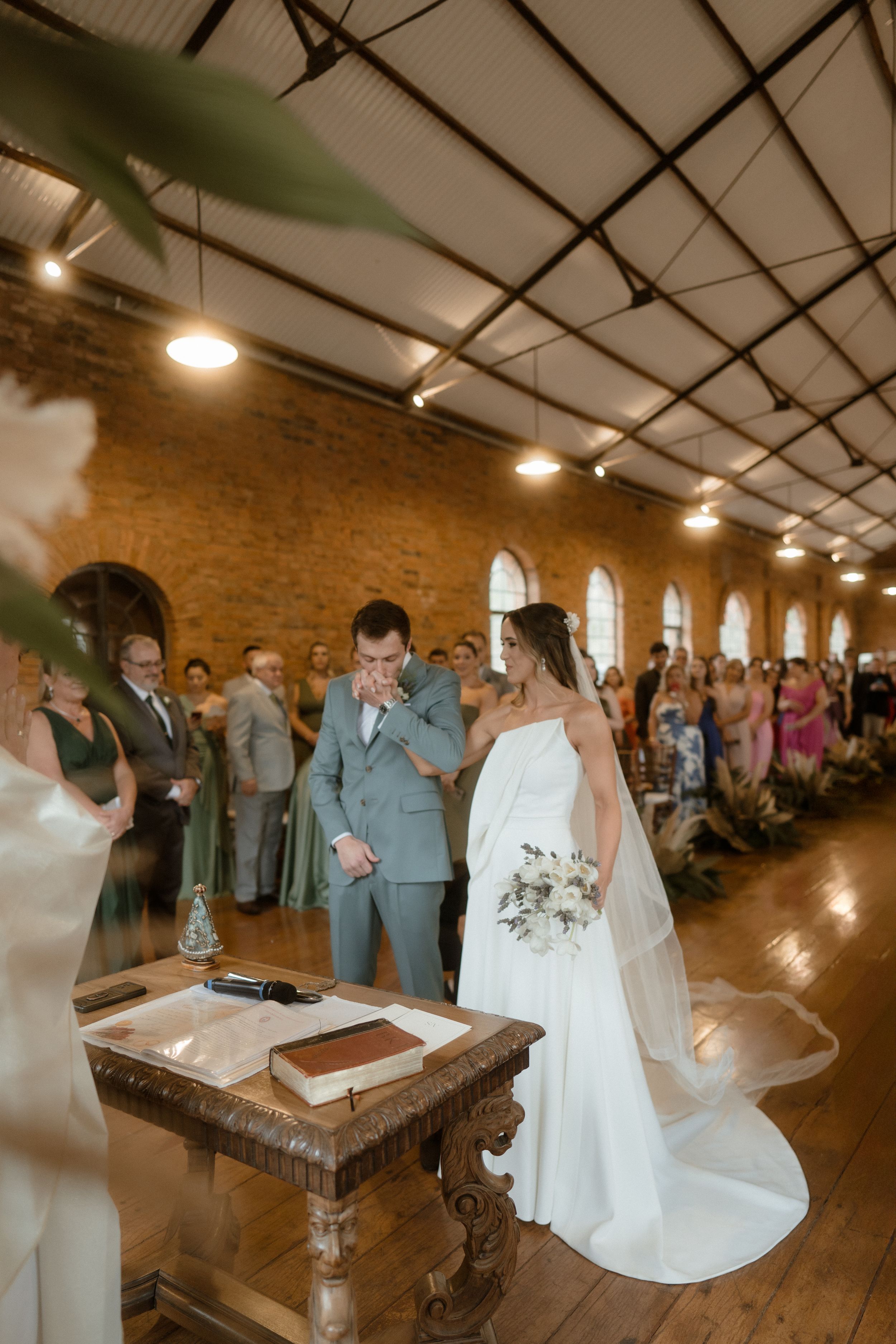 Wedding ceremony in rustic brick venue with couple standing at antique wooden table during proceedings.