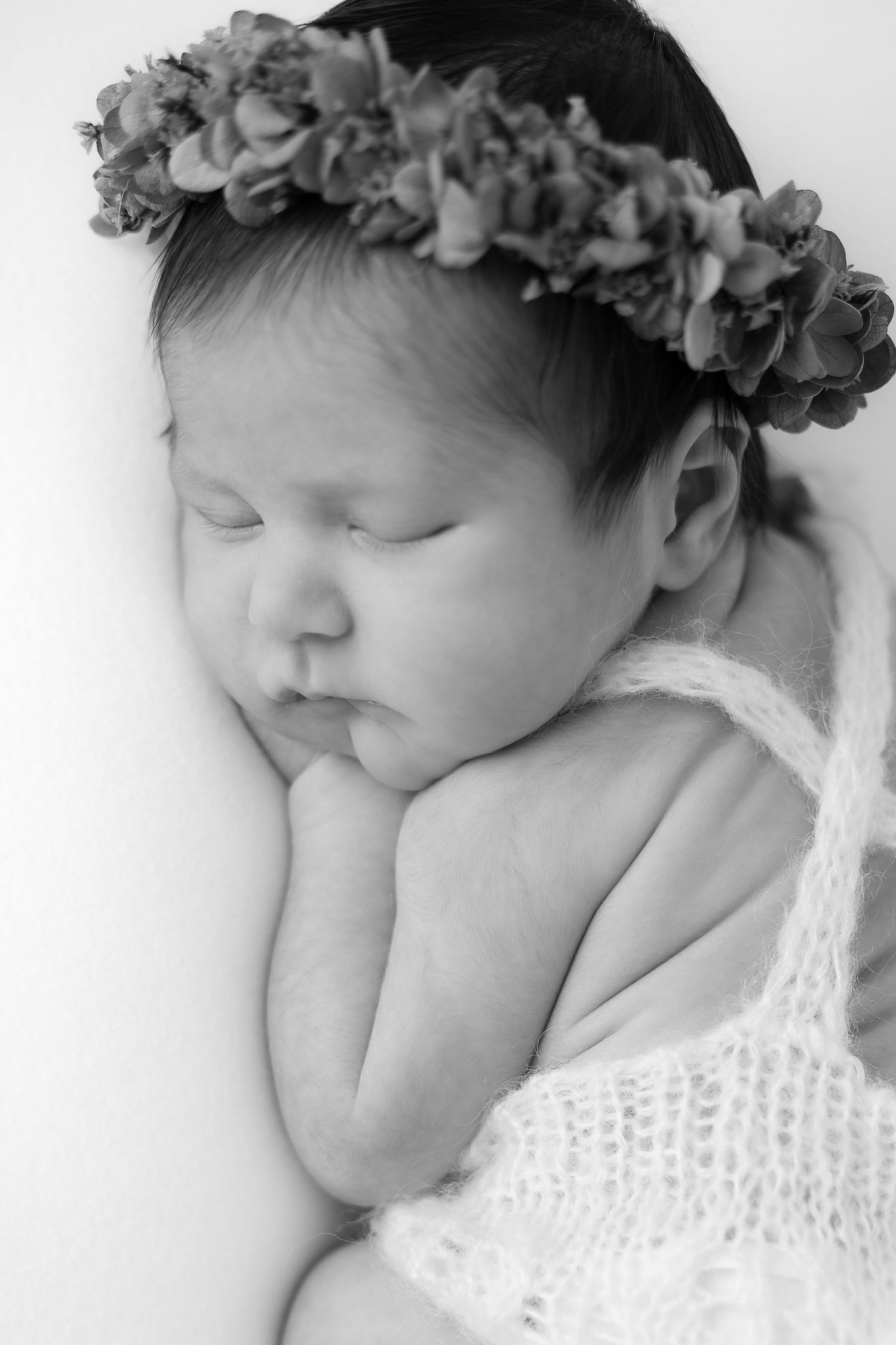 Black and white portrait of sleeping baby wearing delicate lace wrap and floral crown.