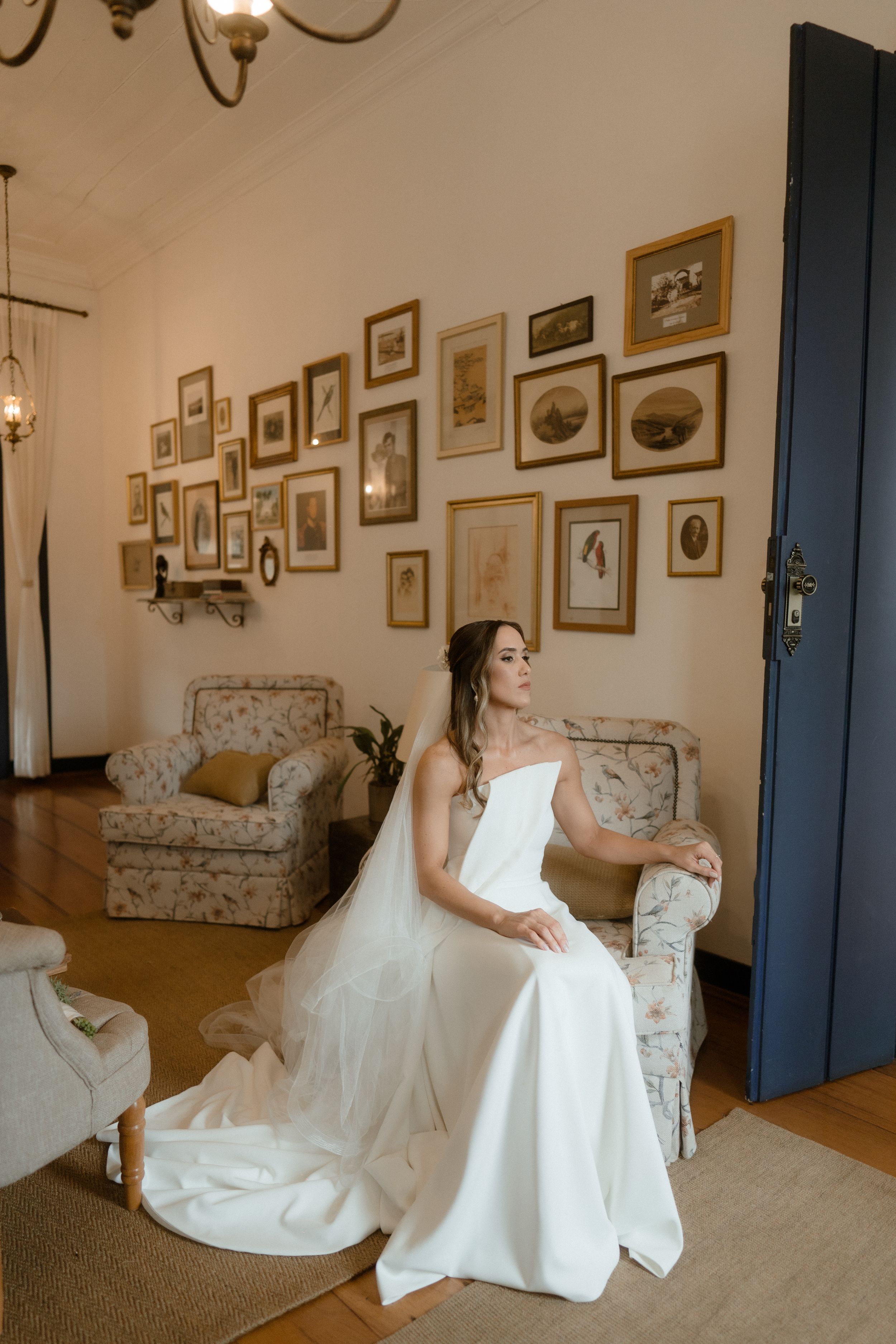 Bride in white gown poses gracefully on vintage furniture in a warmly lit room.
