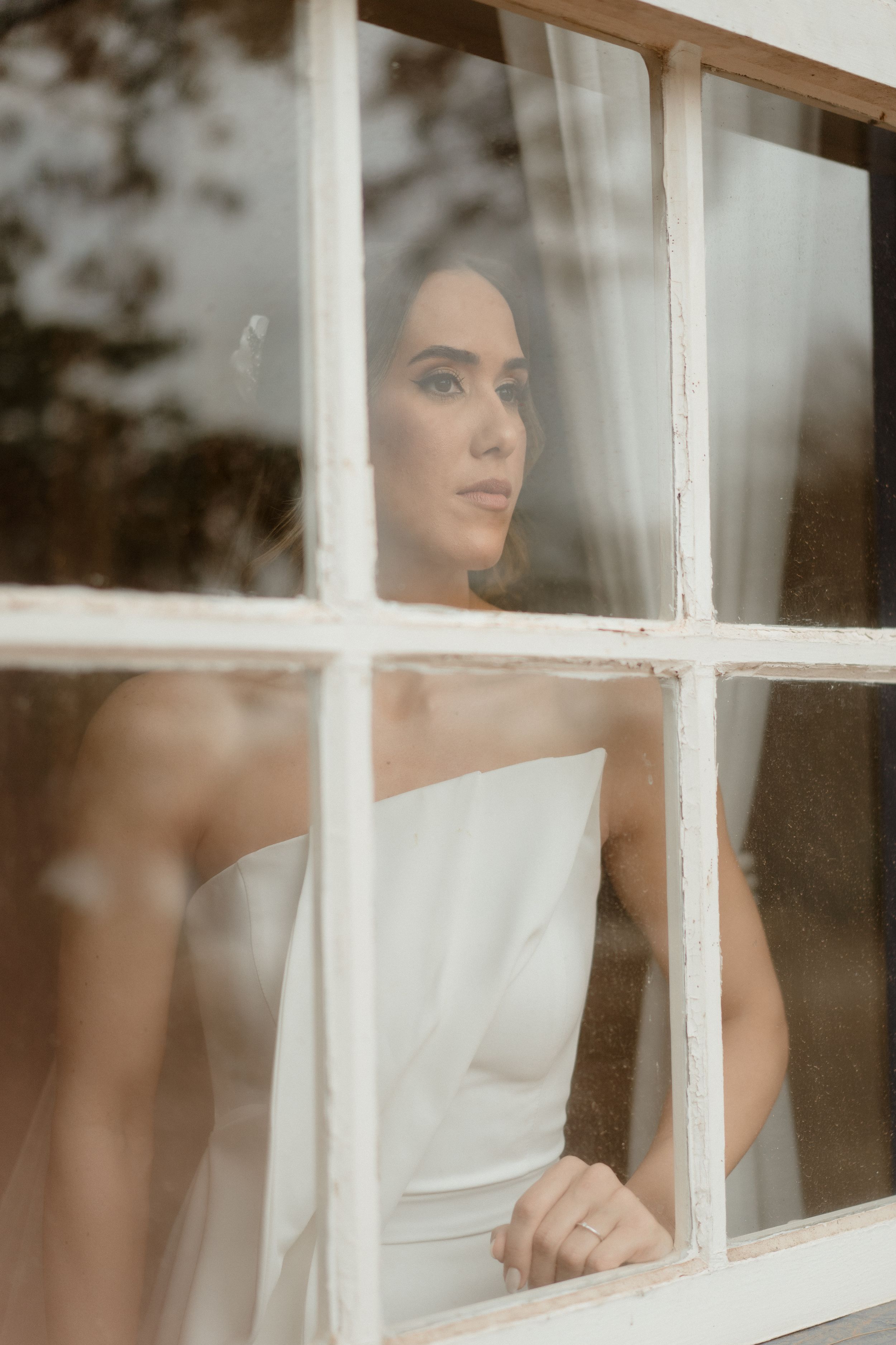Artistic bridal portrait through windowpanes creating a romantic, vintage aesthetic.
