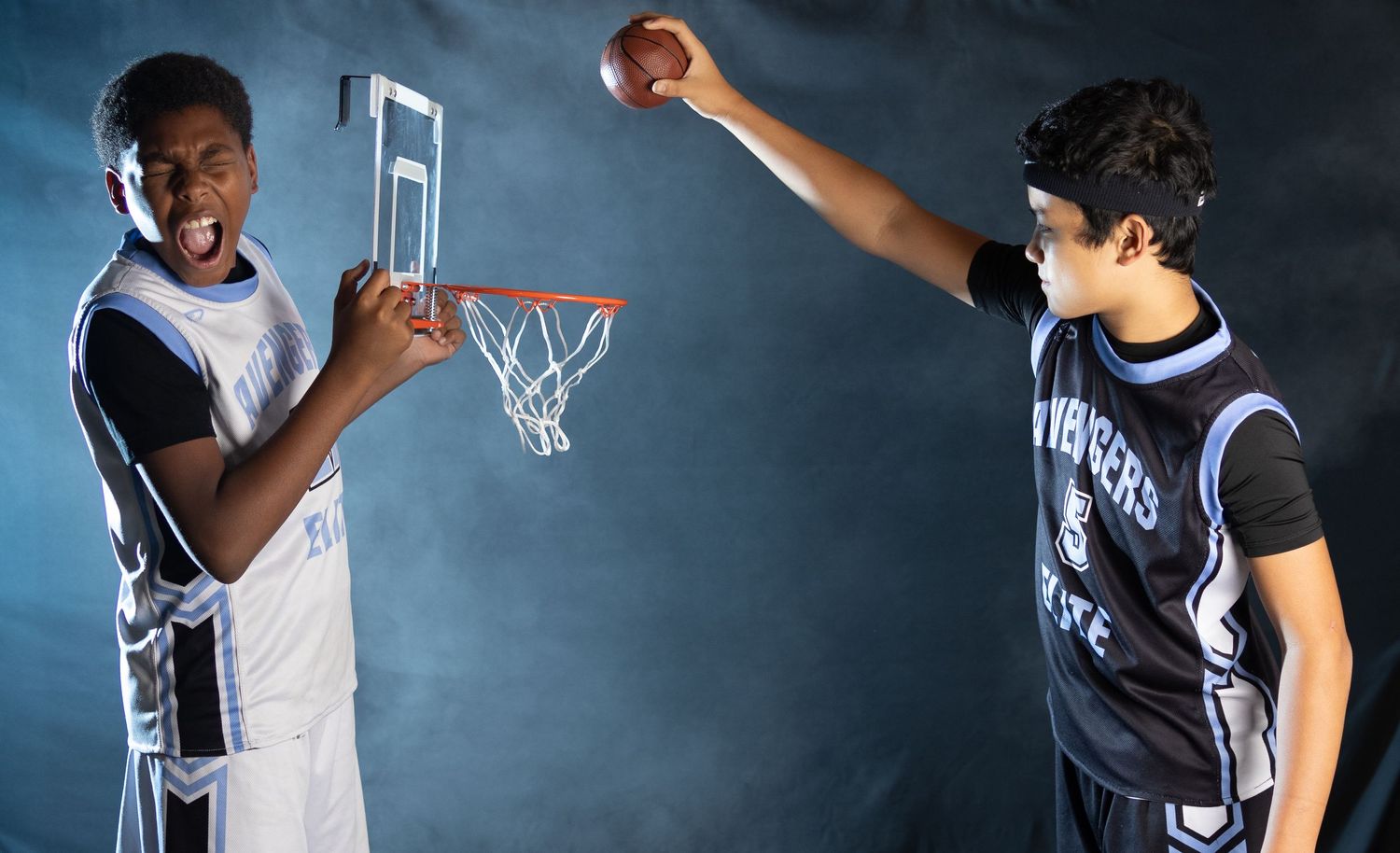 Two basketball players face off in dramatic lighting, one holding a tiny hoop while the other prepares to shoot.
