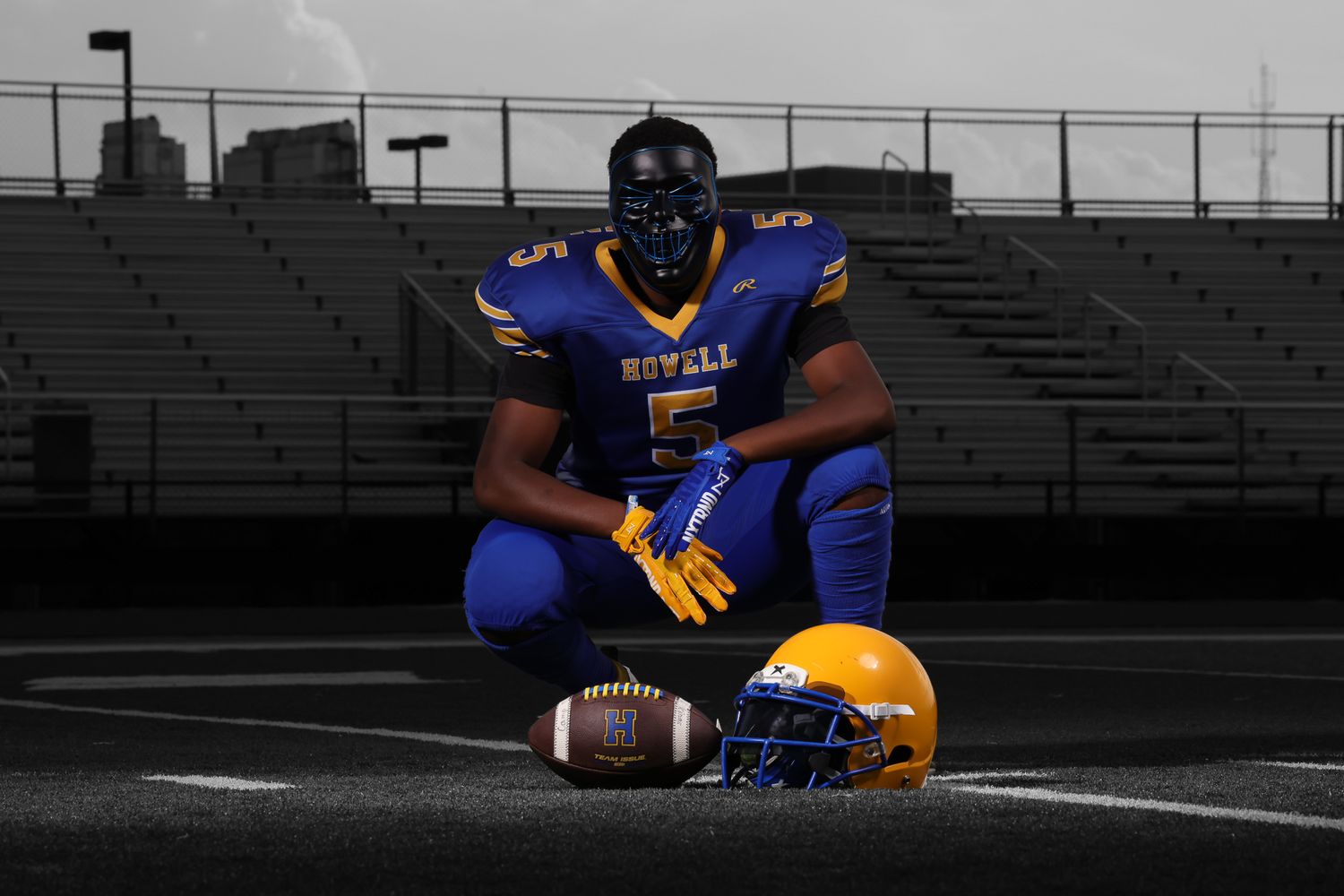 Football player in blue and gold uniform crouches on field ready for action during practice session.