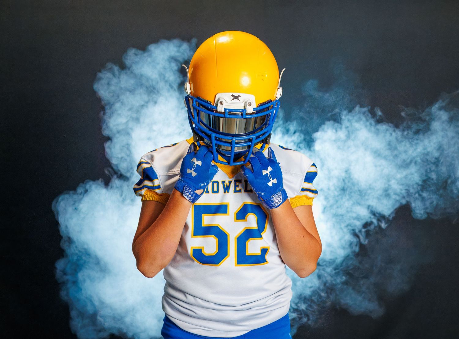 Football player in white and blue uniform number 52 poses in dramatic blue smoke against dark background.
