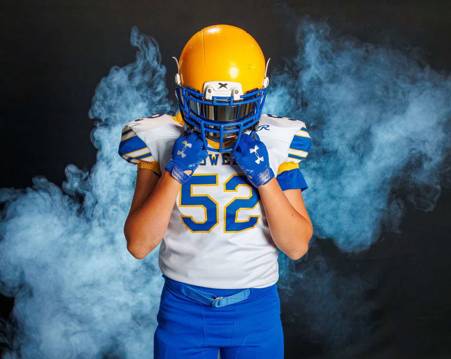 Football player in uniform number 52 poses with dramatic blue smoke effect and dark backdrop.