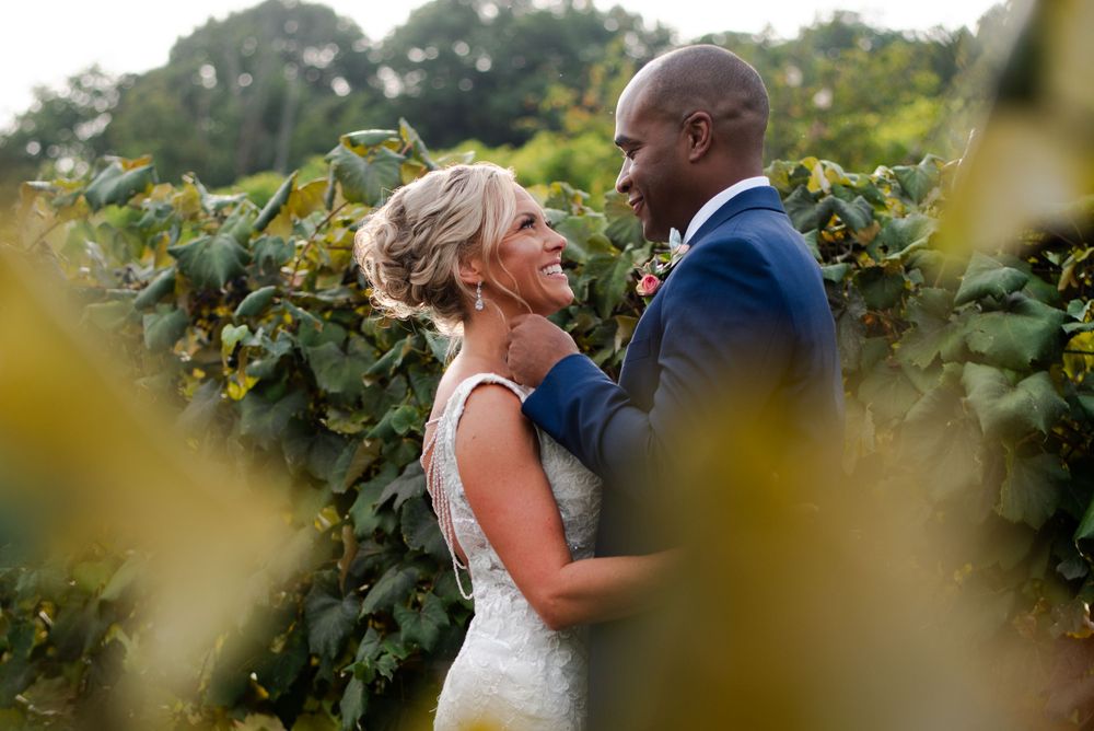 A couple embraces among lush green grapevines during photos at the vineyard.