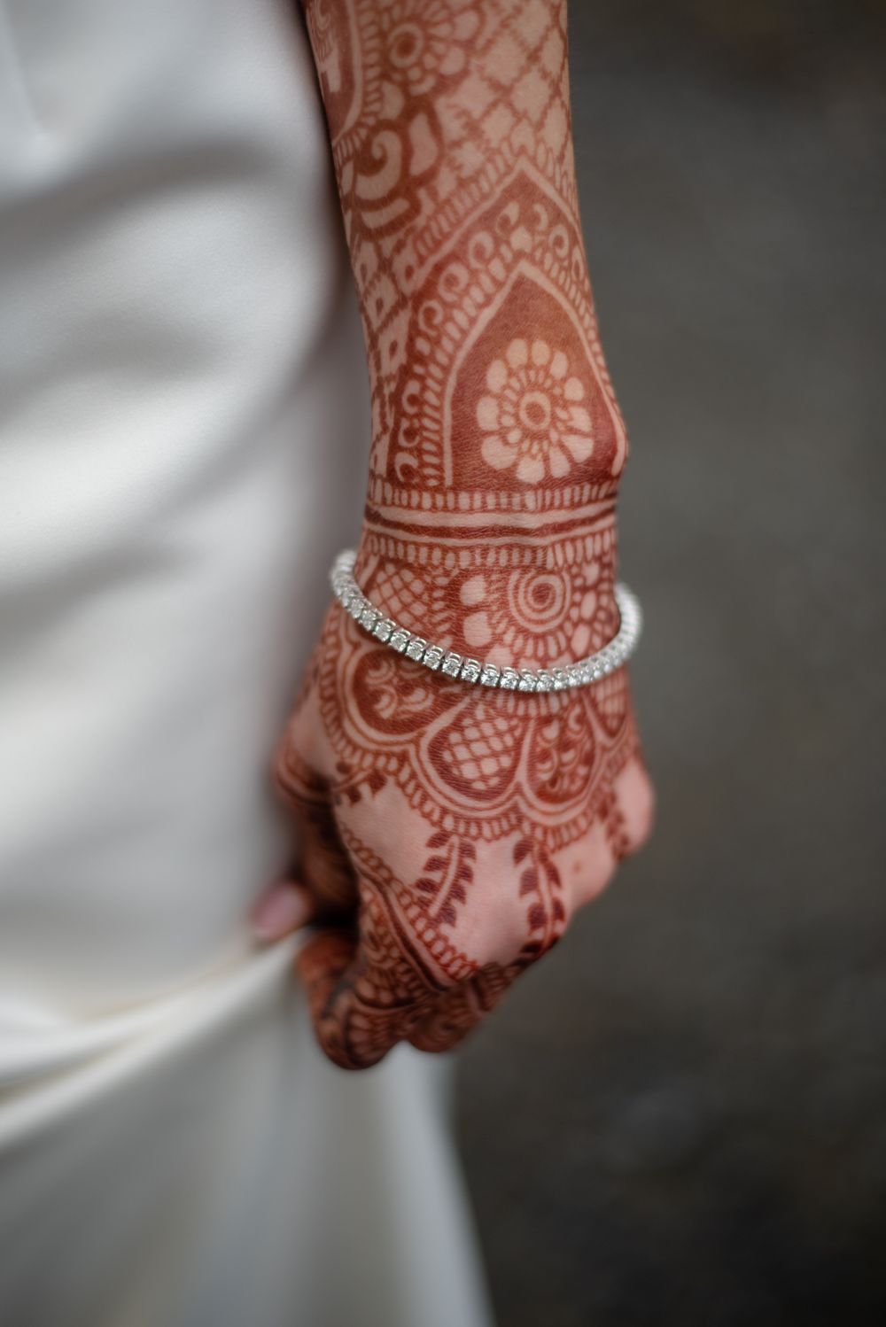 Close-up photo of bridal mehndi the brides beautiful tennis bracelet as she gently holds her gown.
