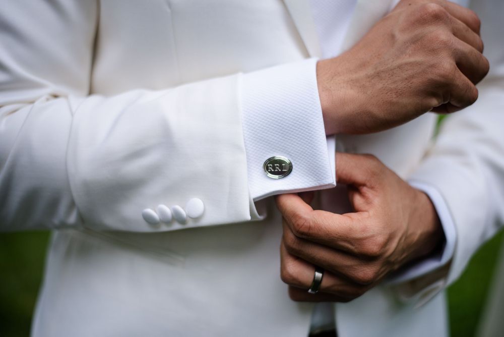 Close-up view of hands adjusting a silver cufflink on crisp white tux sleeve.