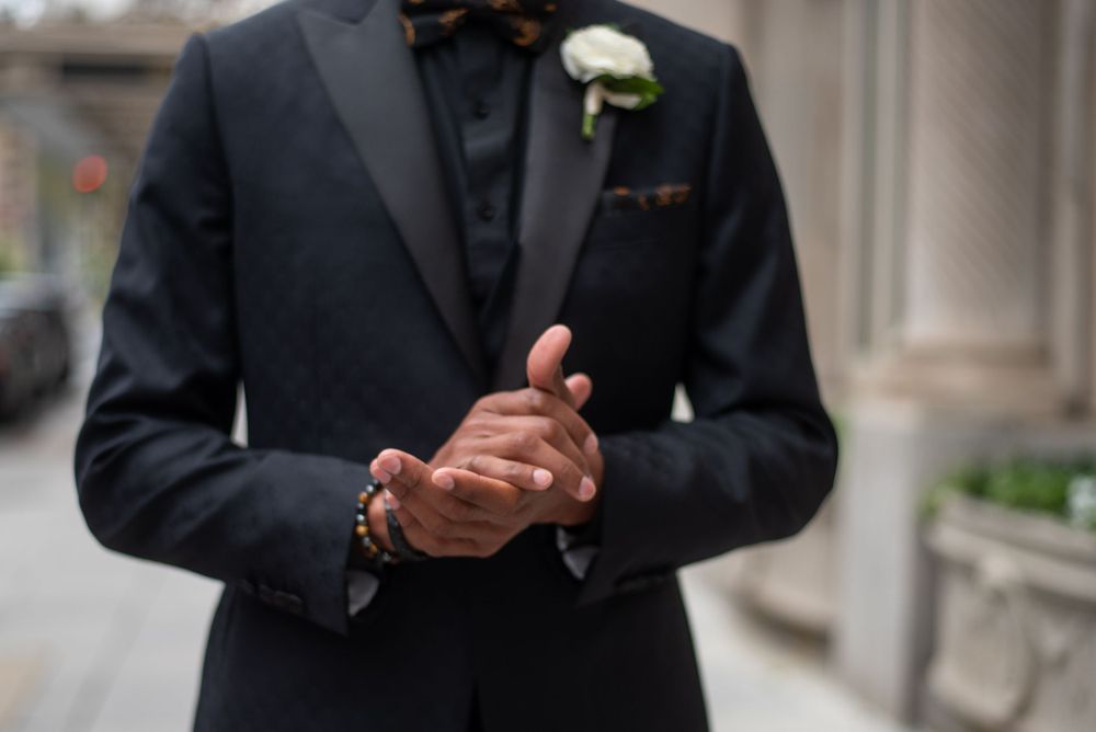 Groom pressing his hands together posing for portraits outside hotel
