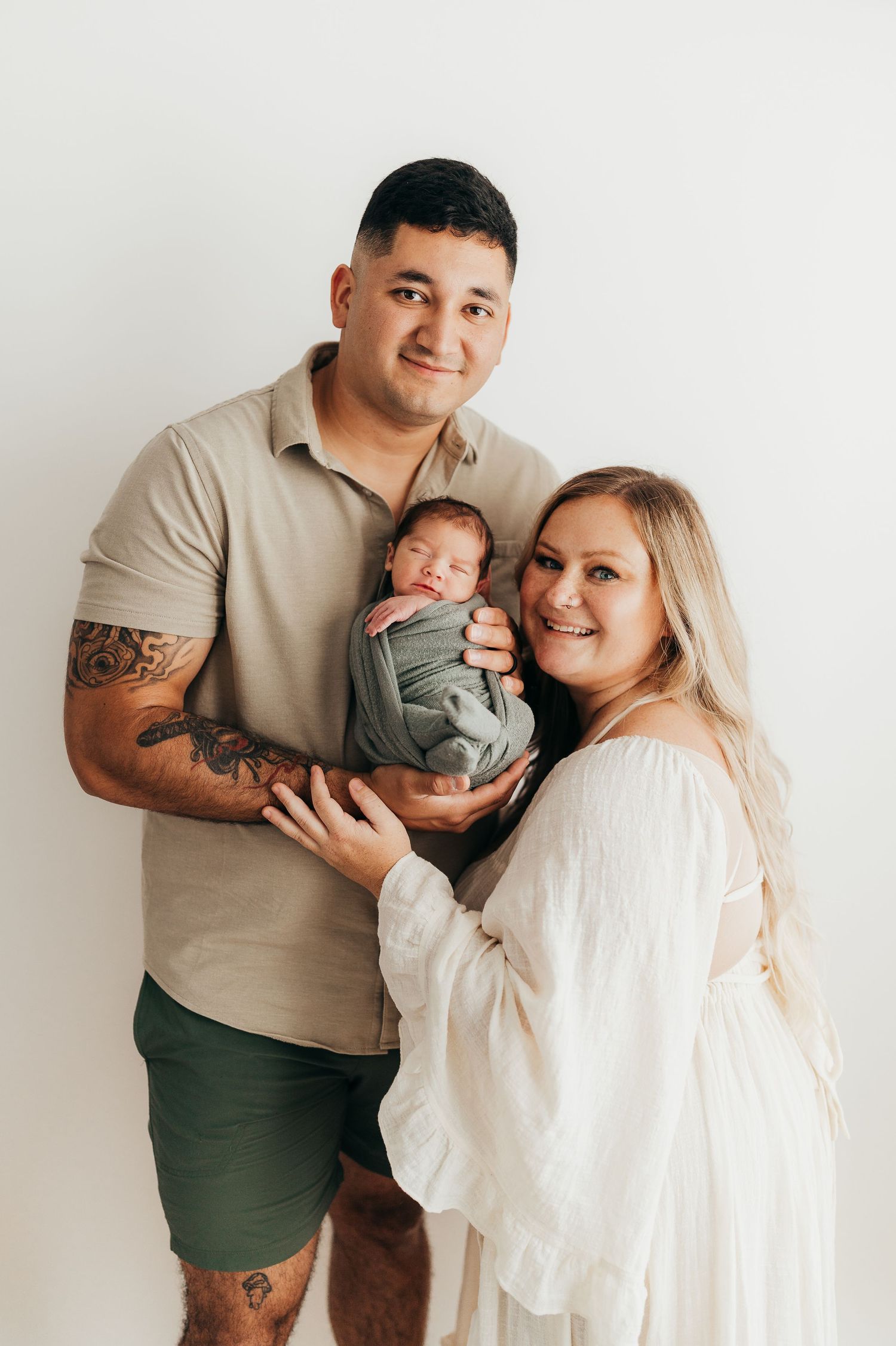 Young family sharing a tender moment together on a beige background. Roscoe IL newborn photographer