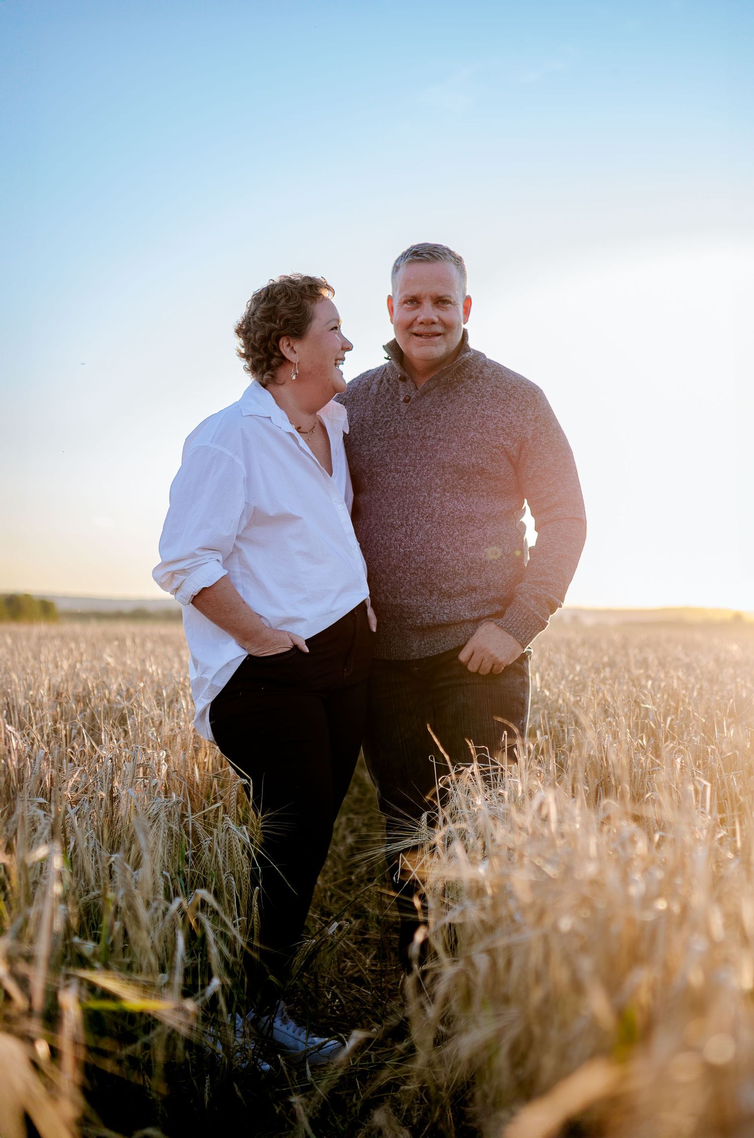 Couple standing close together in a wheat field during sunset.