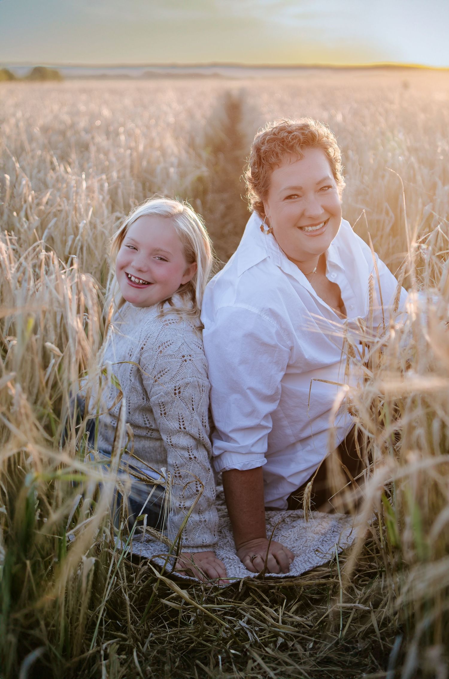 Parent and child sharing a joyful moment together in a wheat field at sunset.