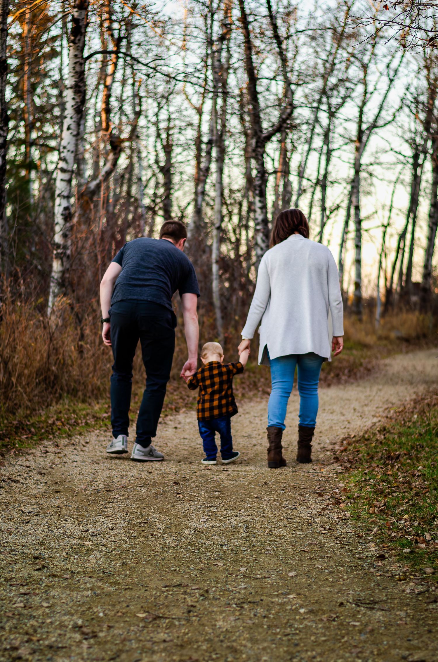 Three people walk hand in hand down a forest trail during autumn.