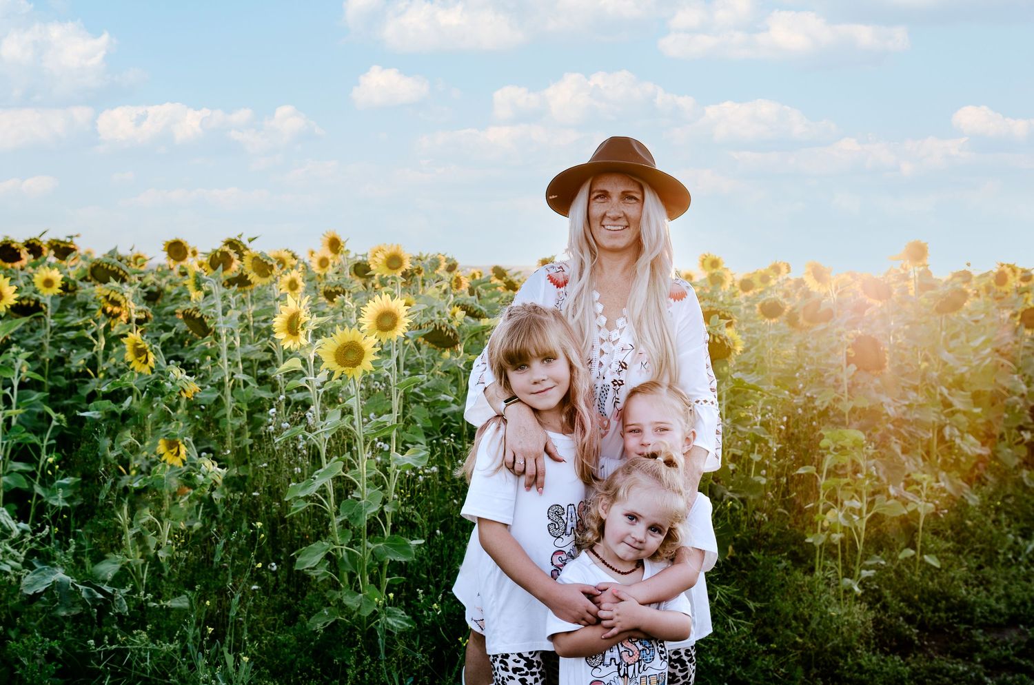 Family group standing together in a vibrant sunflower field during golden hour with sunlight streaming behind them.