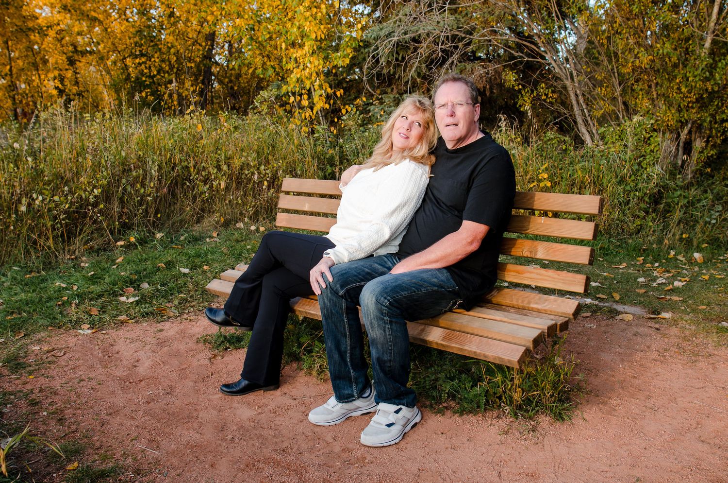 Couple sitting together on wooden park bench surrounded by fall foliage.